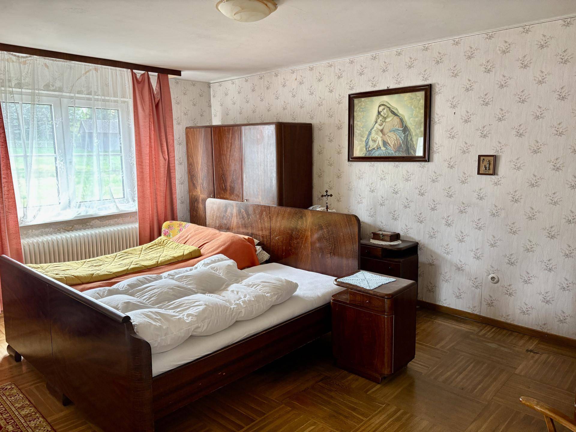 Schlafzimmer mit einem klassischen Holzbett, Kleiderschrank und gemusterter Tapete, strahlt eine gemütliche Atmosphäre aus.