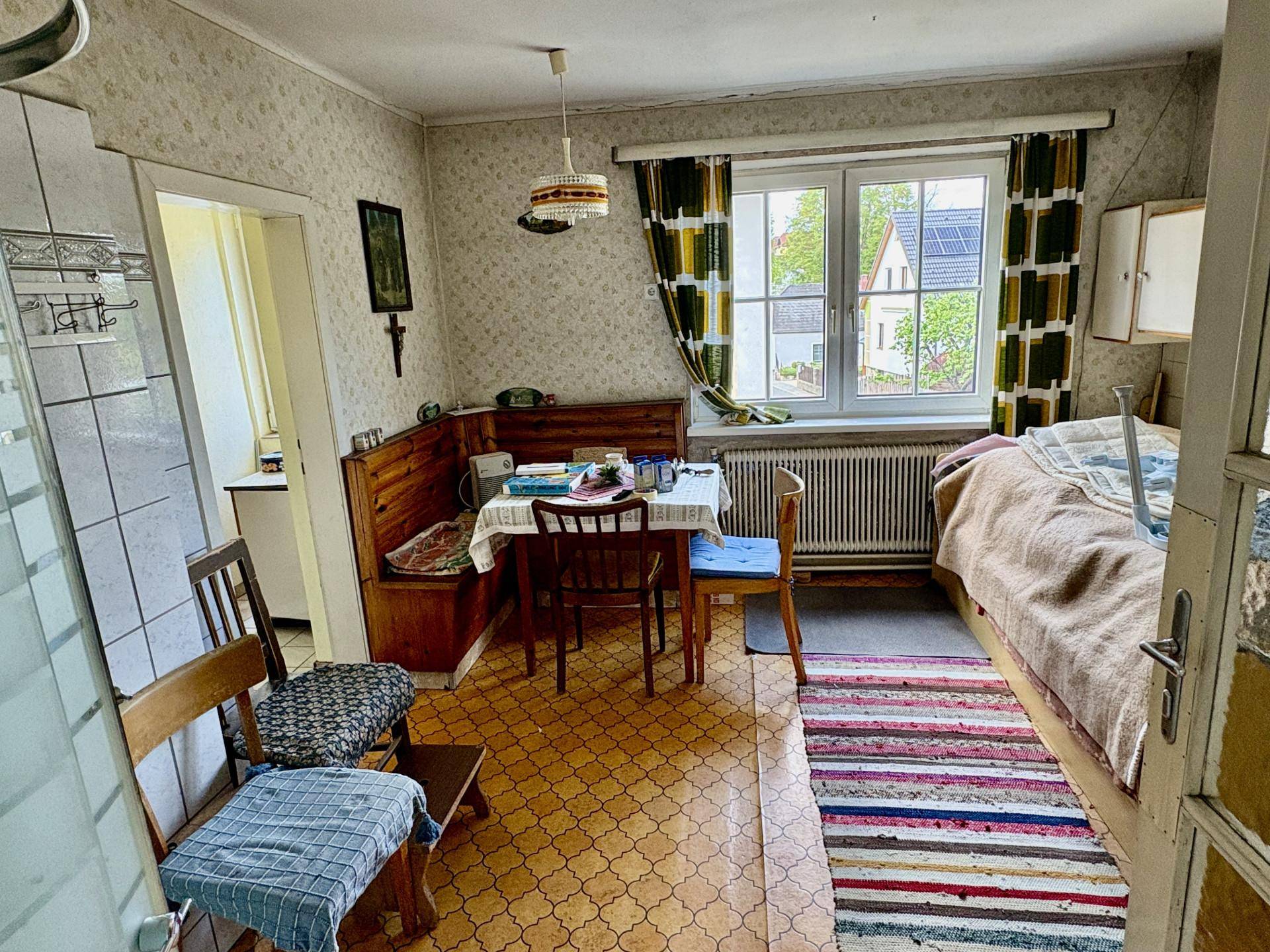 Kombinierter Wohn- und Essbereich mit Bett, Esstisch und gemusterter Tapete, bietet vielseitige Nutzungsmöglichkeiten.
