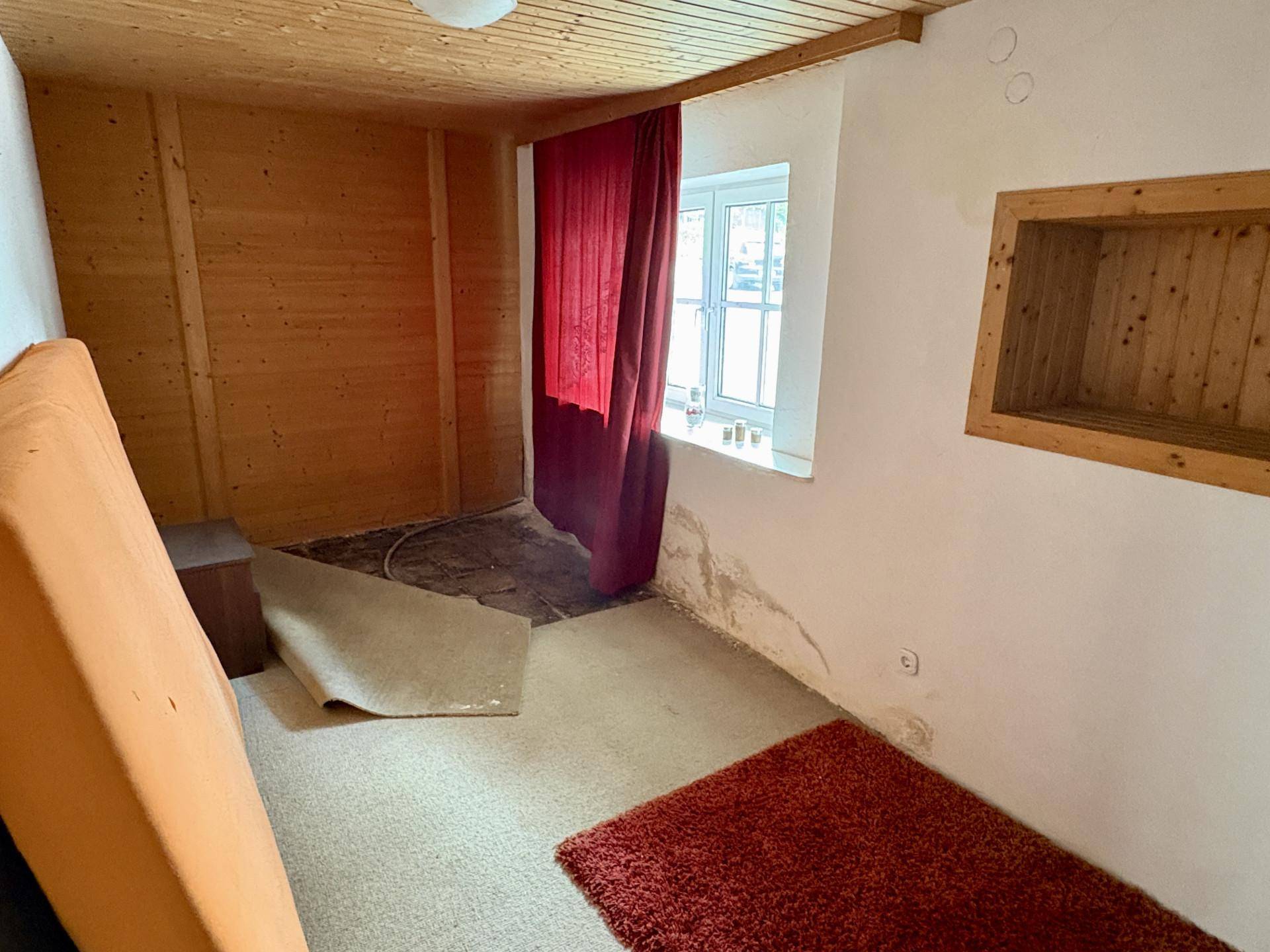 Renovierungsbedürftiger Raum mit Holzvertäfelung, Teppichboden und einem Fenster, das Tageslicht spendet.