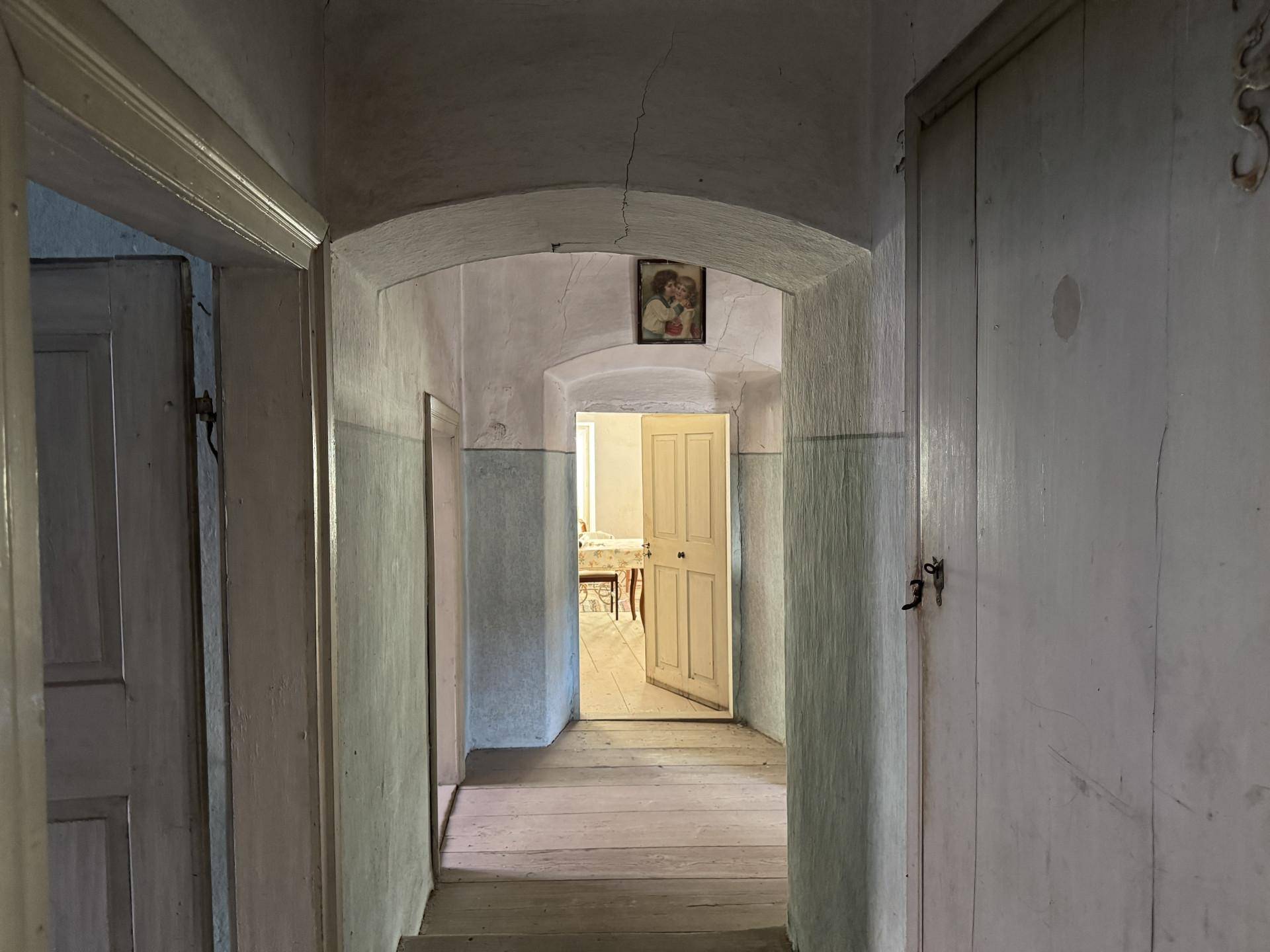 Langer, schmaler Flur mit gewölbten Türrahmen und abgenutztem Holzboden in einem alten Haus.
