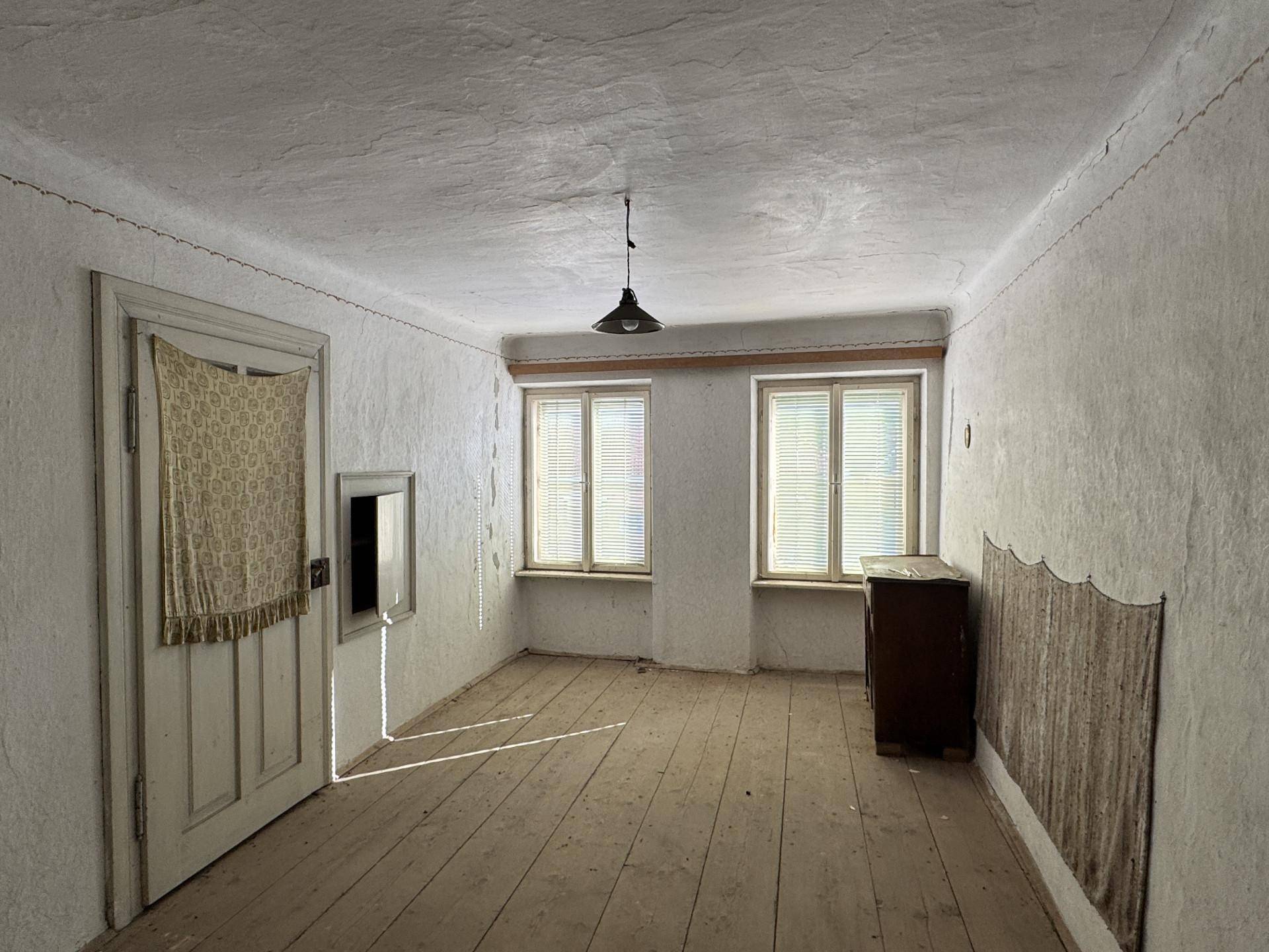 Helles, leeres Zimmer mit weißen Wänden, Holzdielenboden und zwei Fenstern.