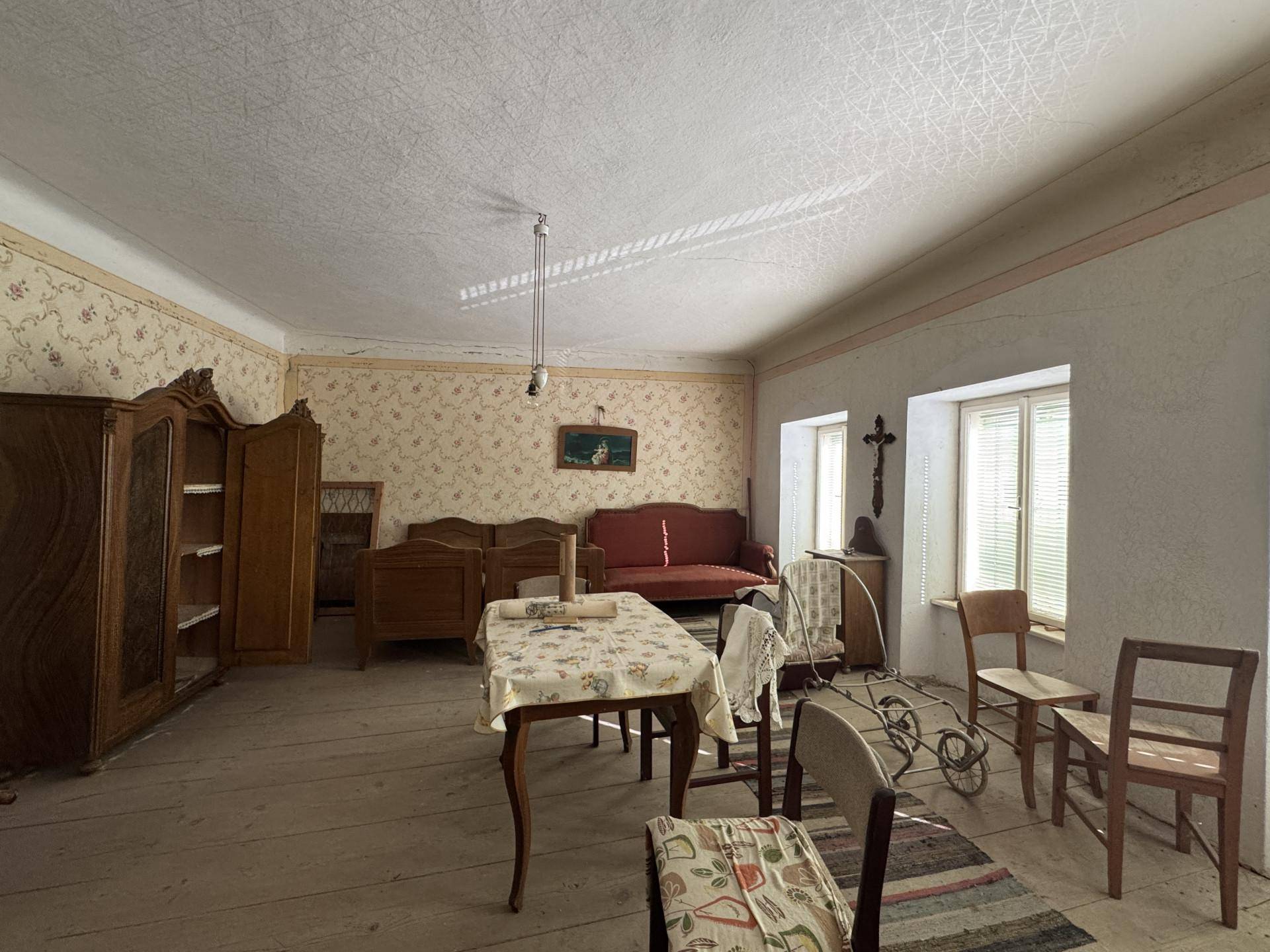 Geräumiges Wohnzimmer mit antiken Möbeln, floraler Tapete und Holzdielenboden.
