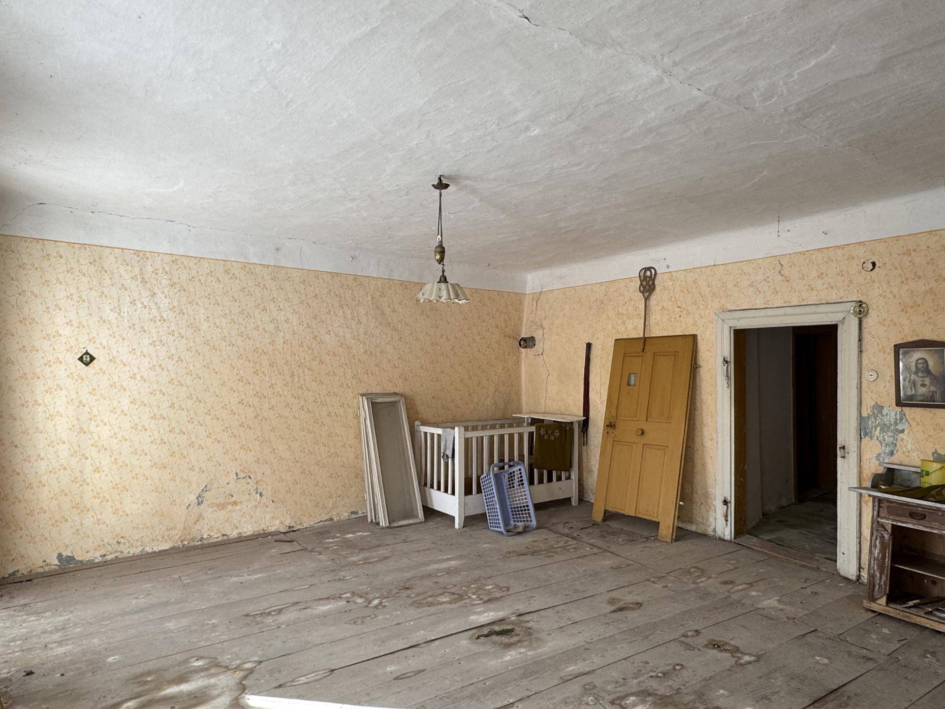 Leeres Schlafzimmer mit alter Tapete, Holzdielenboden und einem Kinderbett in der Ecke.