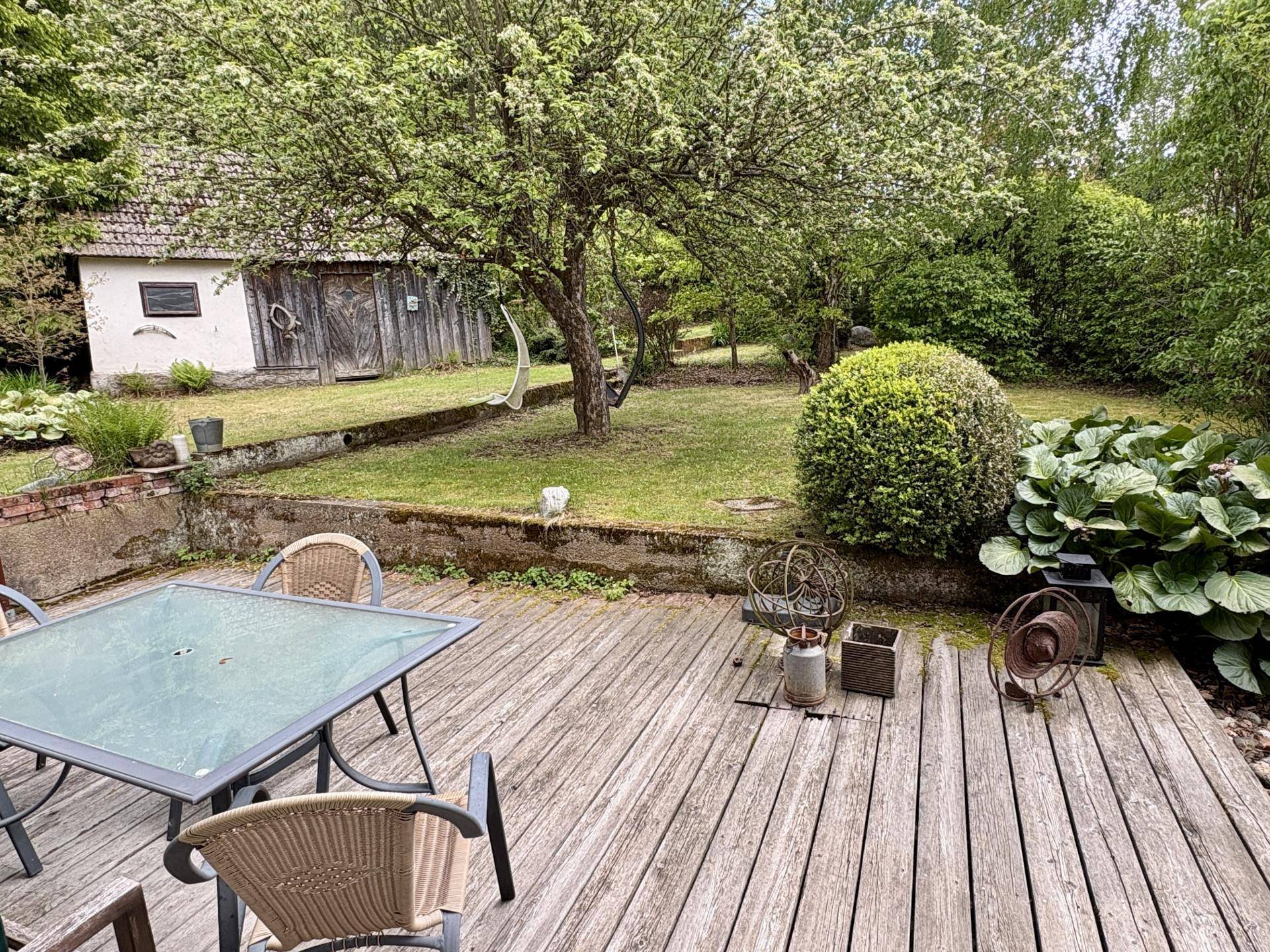 Gemütliche Holzterrasse mit Gartenmöbeln und Blick auf den weitläufigen grünen Garten.