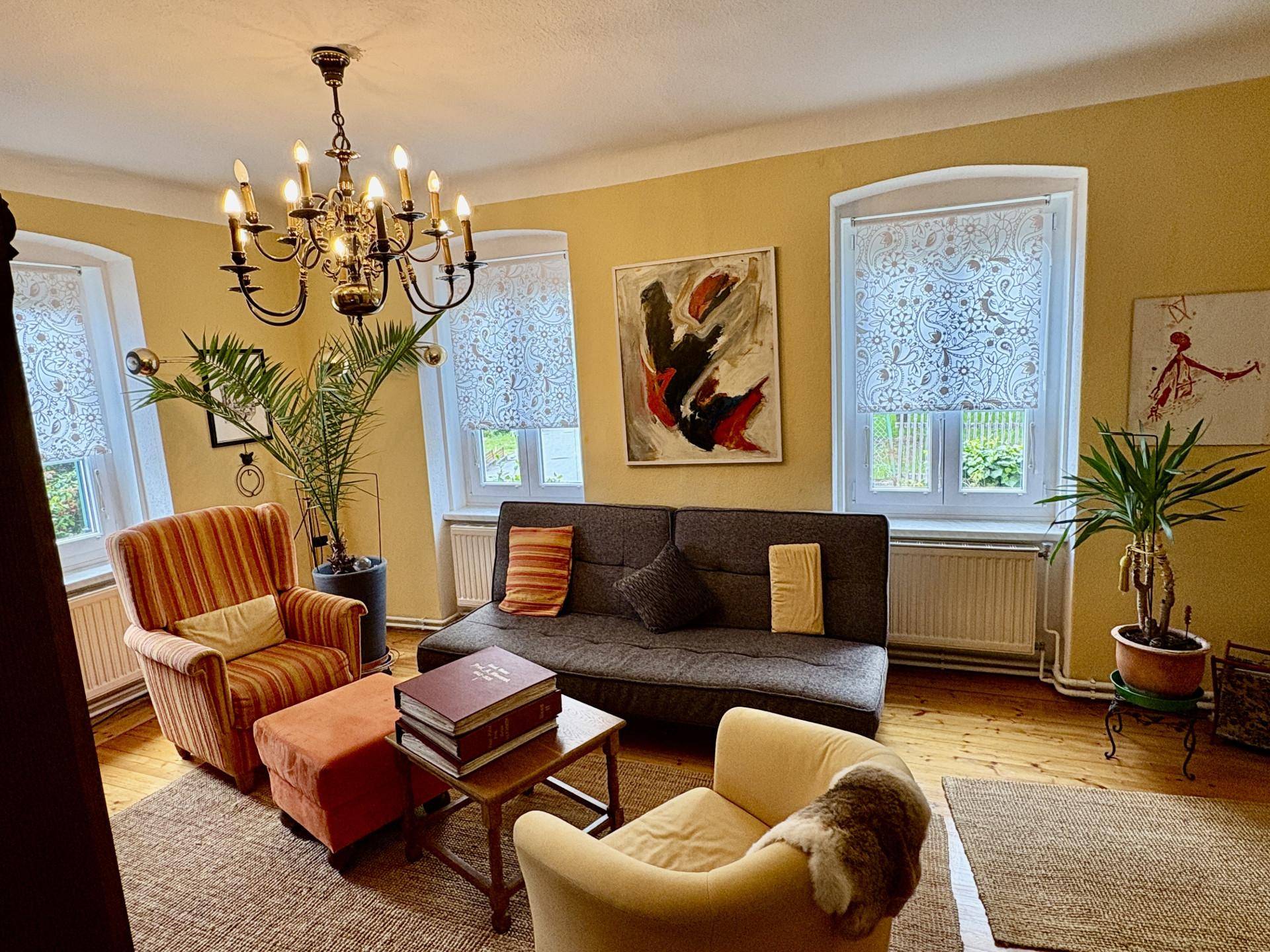 Gemütliches Wohnzimmer mit gelben Wänden, Holzboden und einem klassischen Kronleuchter.