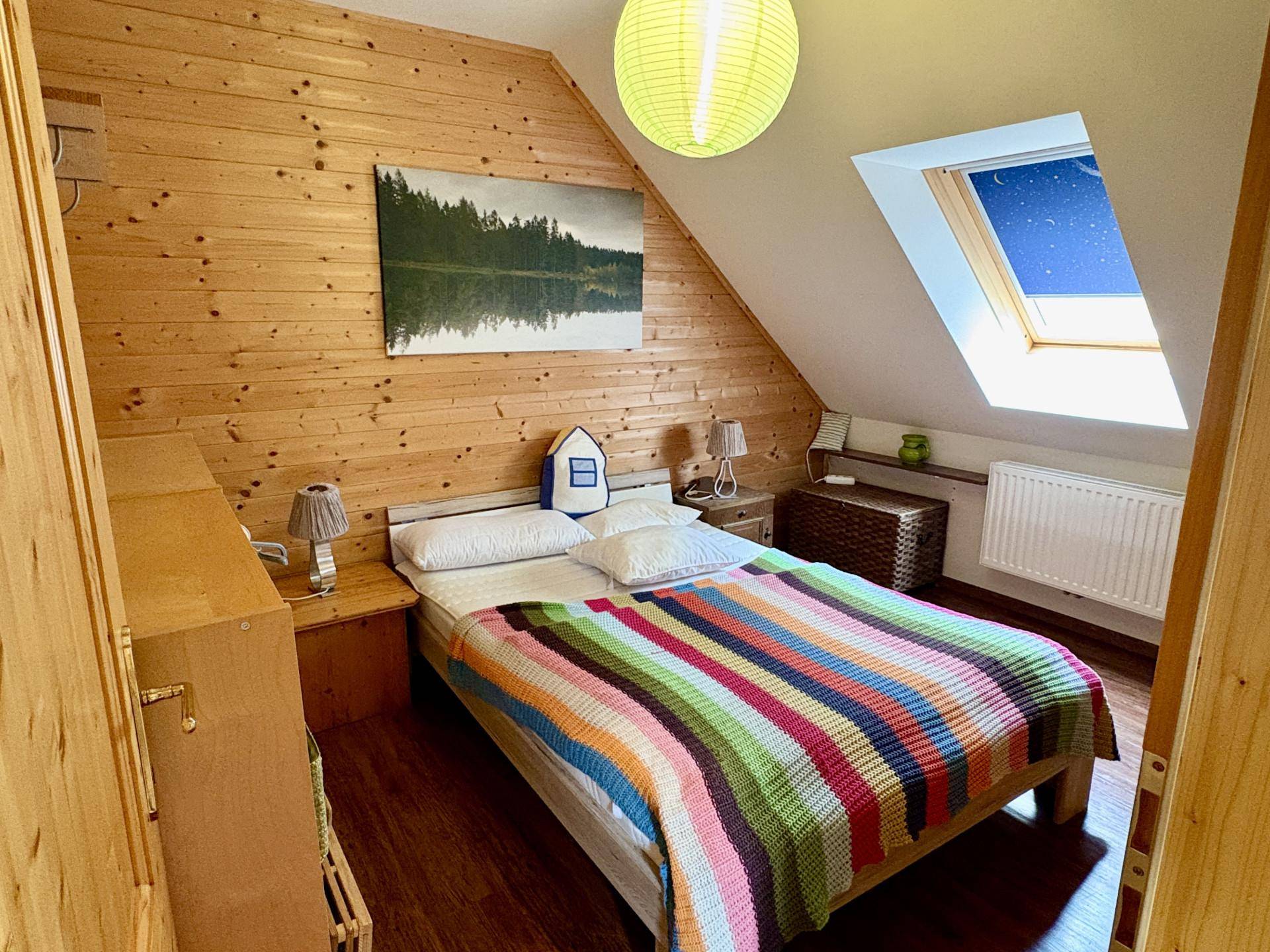 Gemütliches Schlafzimmer im Dachgeschoss mit Holzverkleidung und einem praktischen Dachfenster.