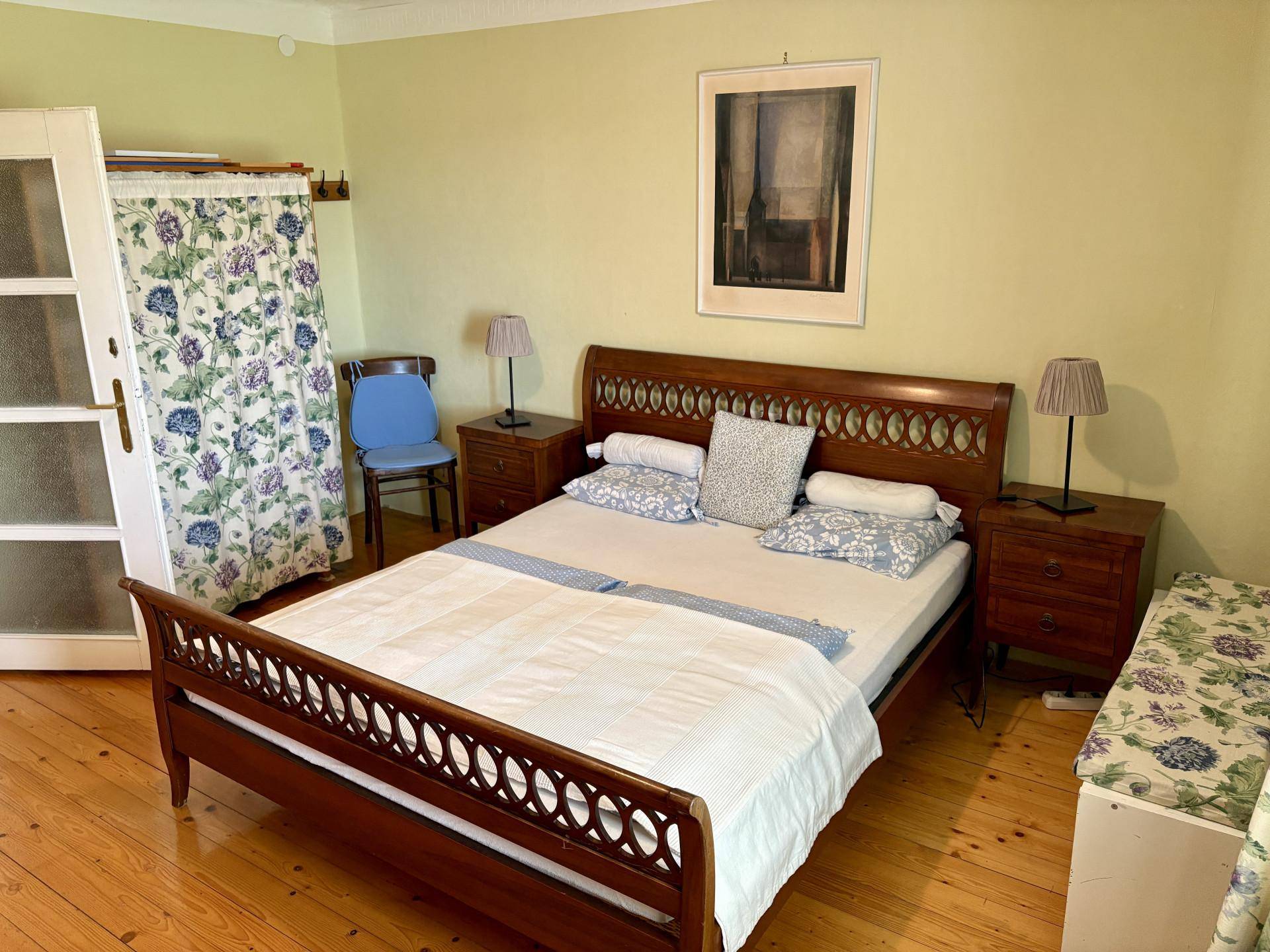 Helles Schlafzimmer mit klassischem Holzbett, gelbgrünen Wänden und Holzboden.
