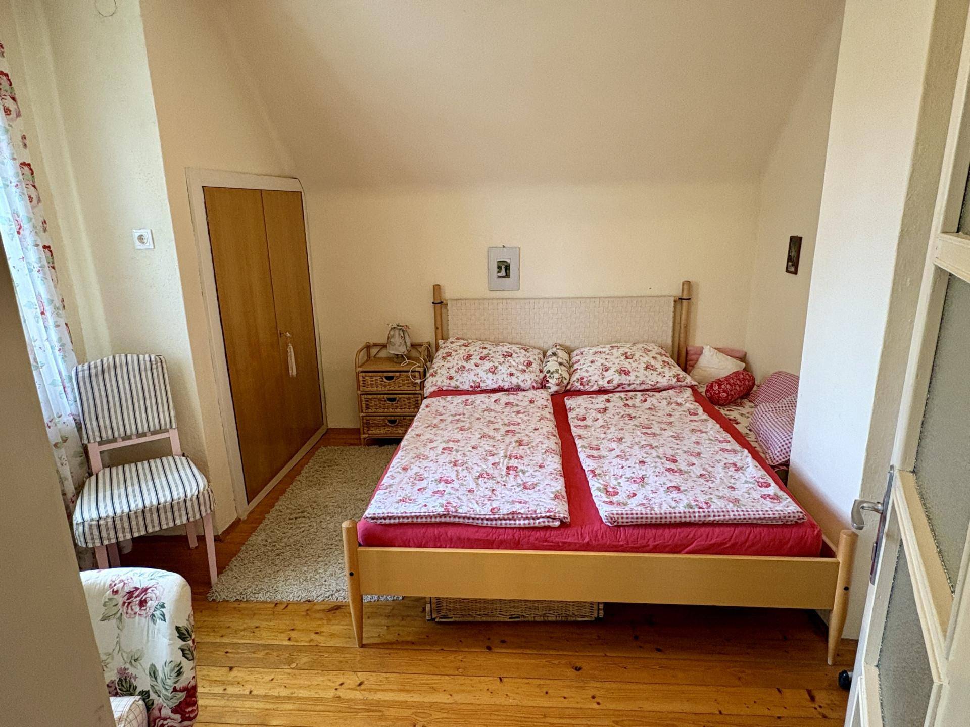 Freundliches Schlafzimmer mit Doppelbett, Holzboden und floralen Mustern auf der Bettwäsche.