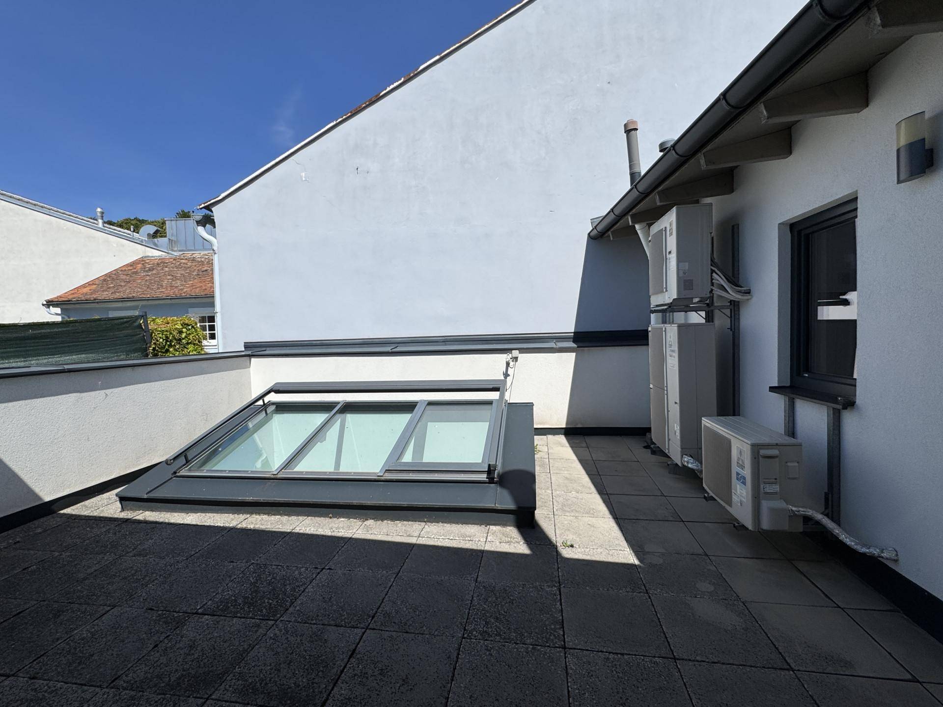 Sonniger Terrassenbereich mit Klimaanlagen-Außengeräten und einem großen Dachfenster.