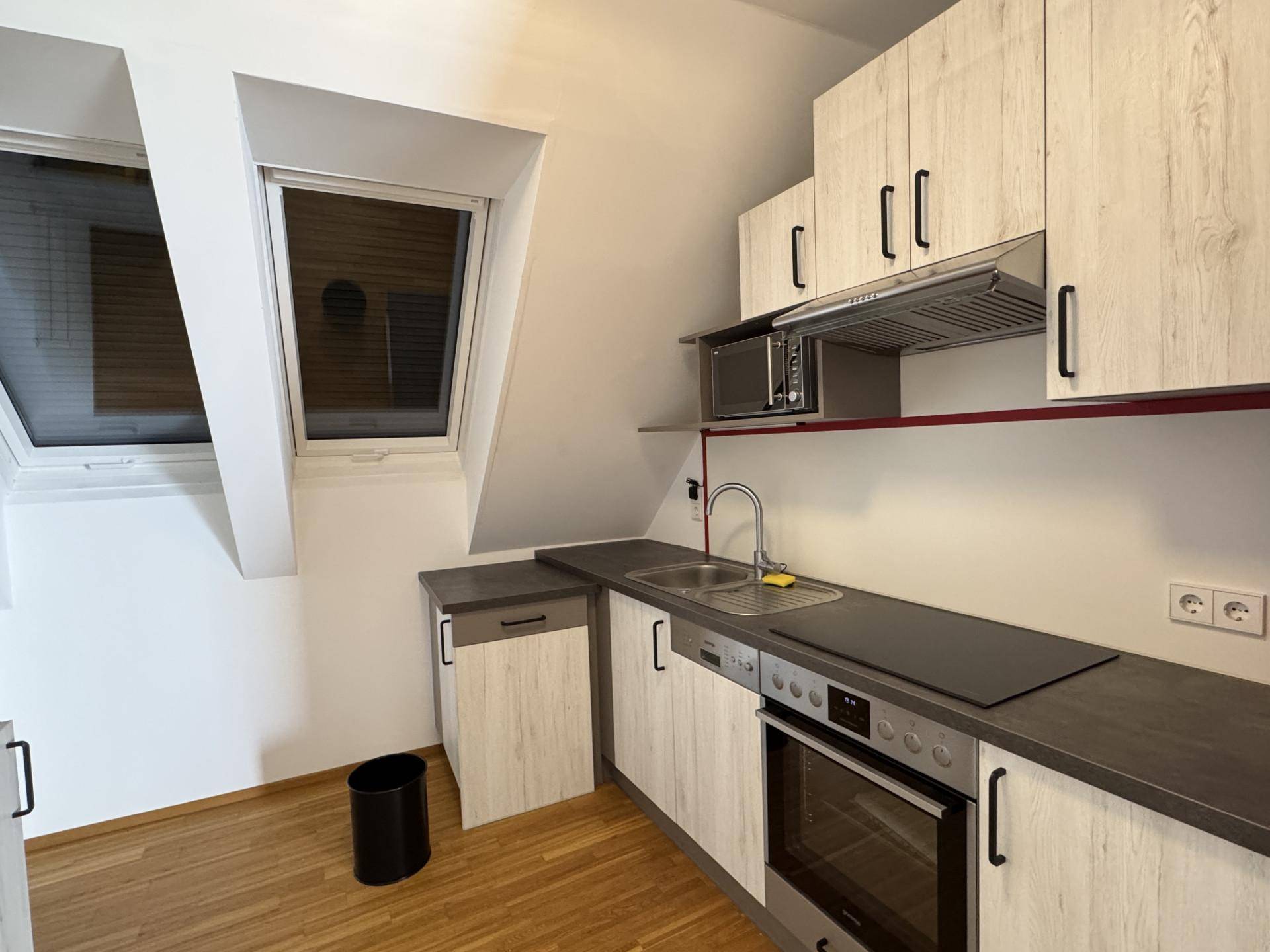 Kleine Einbauküche mit hellen Holzfronten, Dachschrägen und integrierten Geräten.
