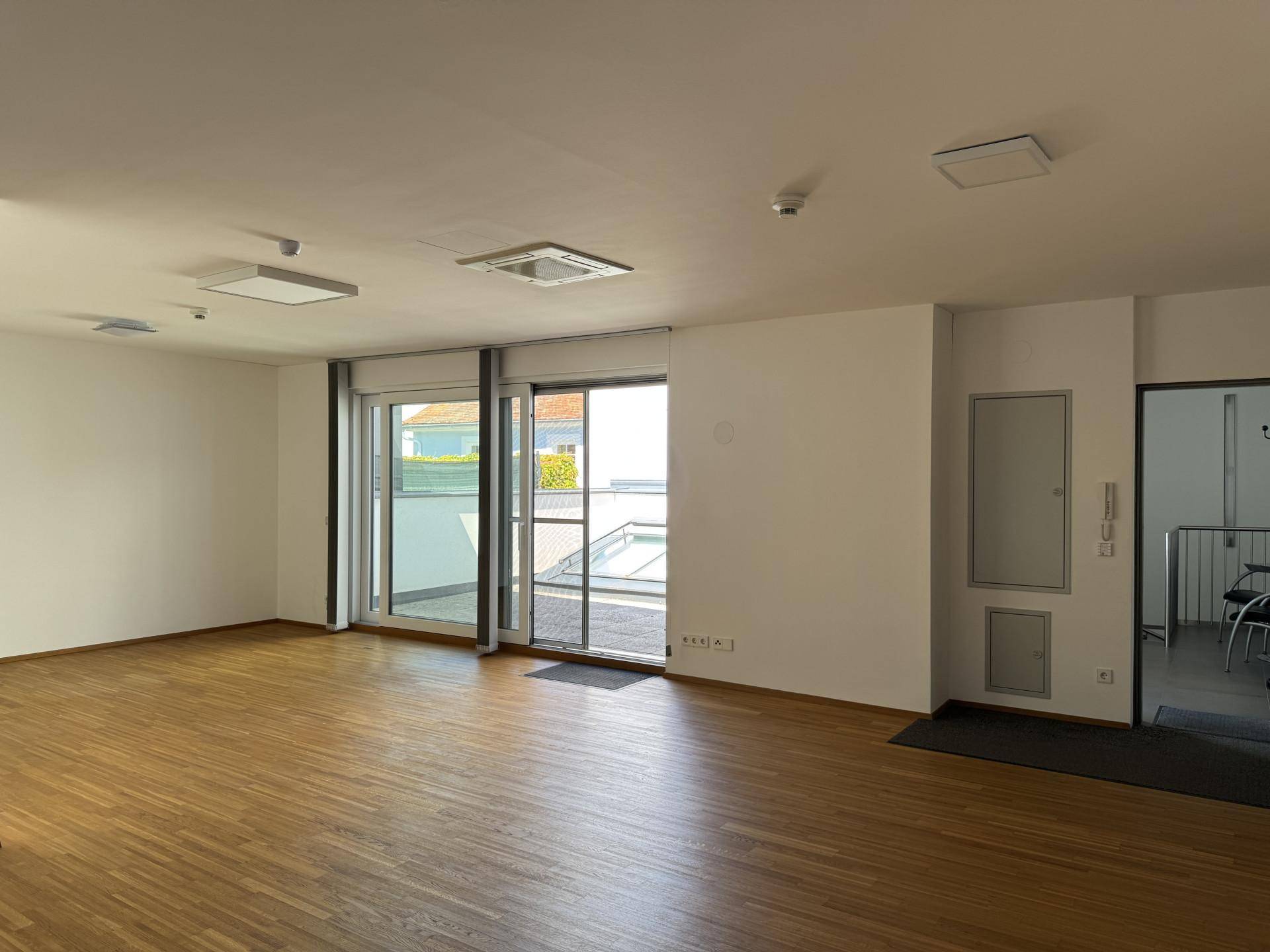 Heller, leerer Wohnraum mit Holzboden und Zugang zu einer Terrasse durch eine Glasschiebetür.