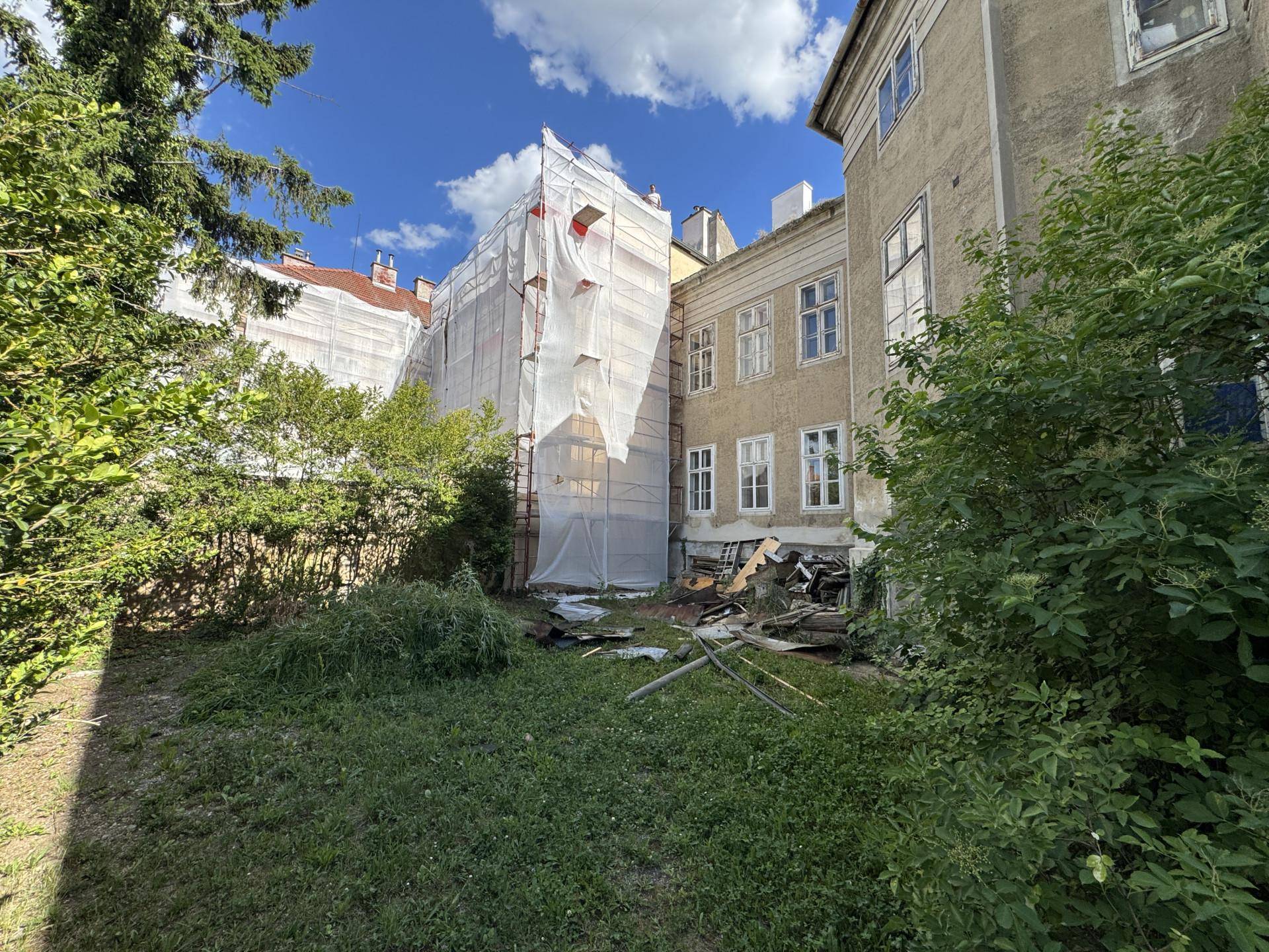 Verwilderter Gartenbereich neben einem Gebäude, das teilweise eingerüstet ist.