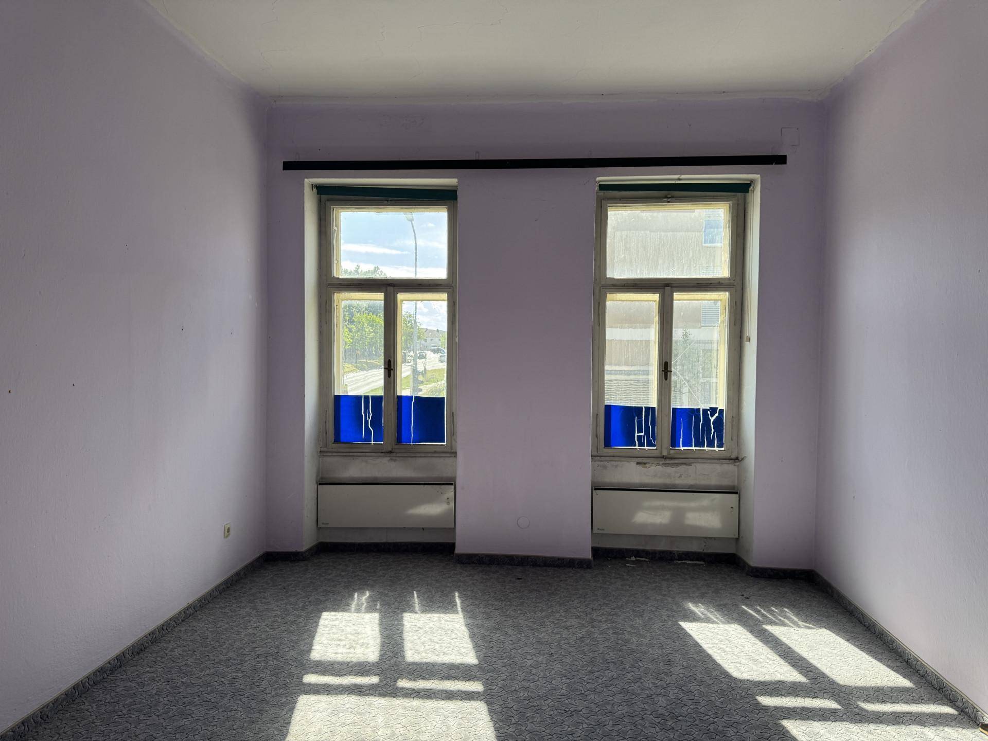 Zimmer mit lila Wänden, Teppichboden und zwei hohen Fenstern.
