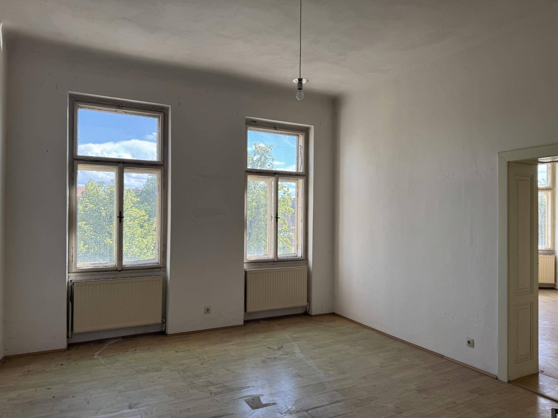 Geräumiges Zimmer mit Holzboden, hohen Fenstern und Blick ins Grüne.