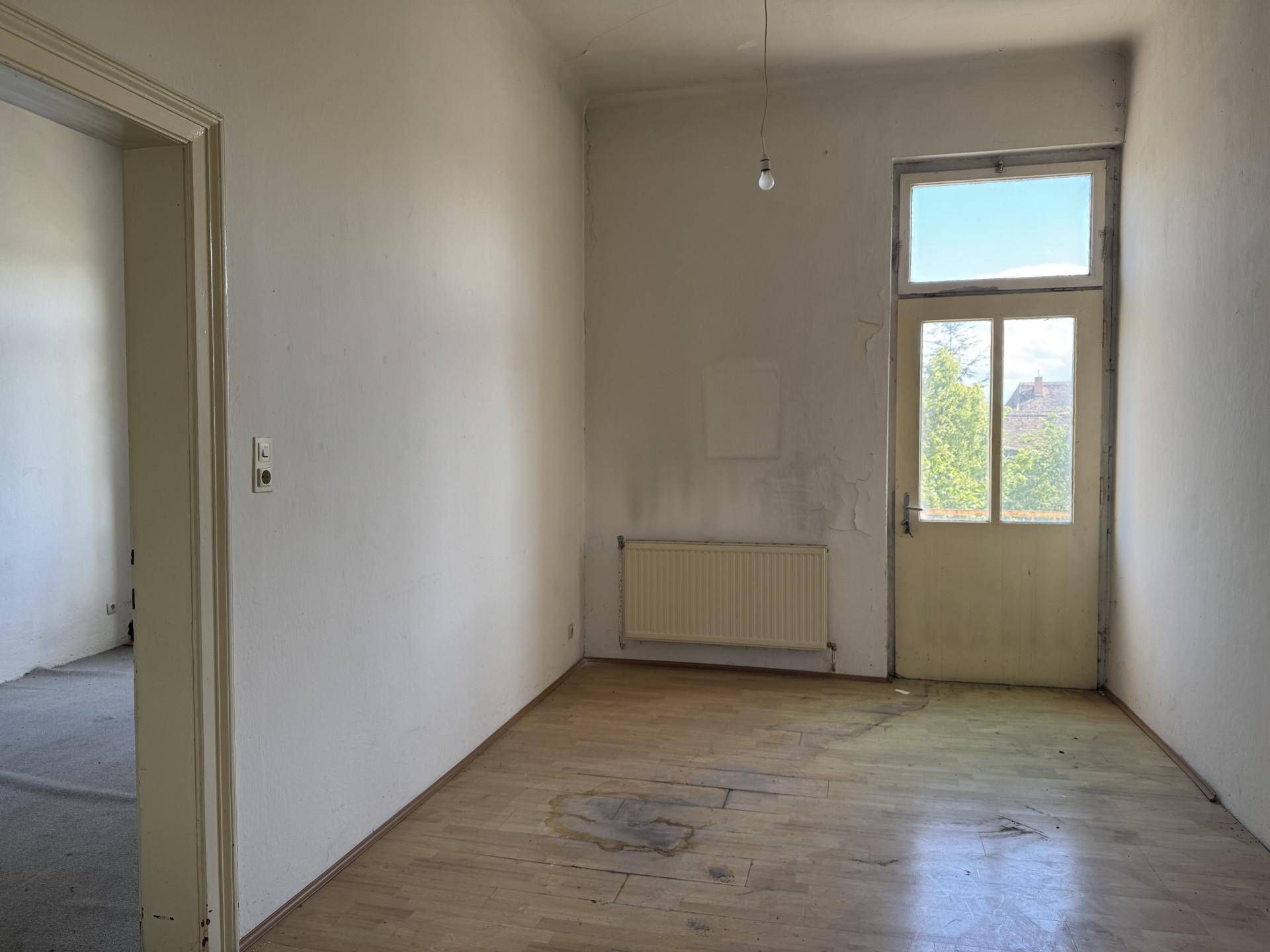 Kleineres Zimmer mit Holzboden, einer Tür nach draußen und Heizkörper.