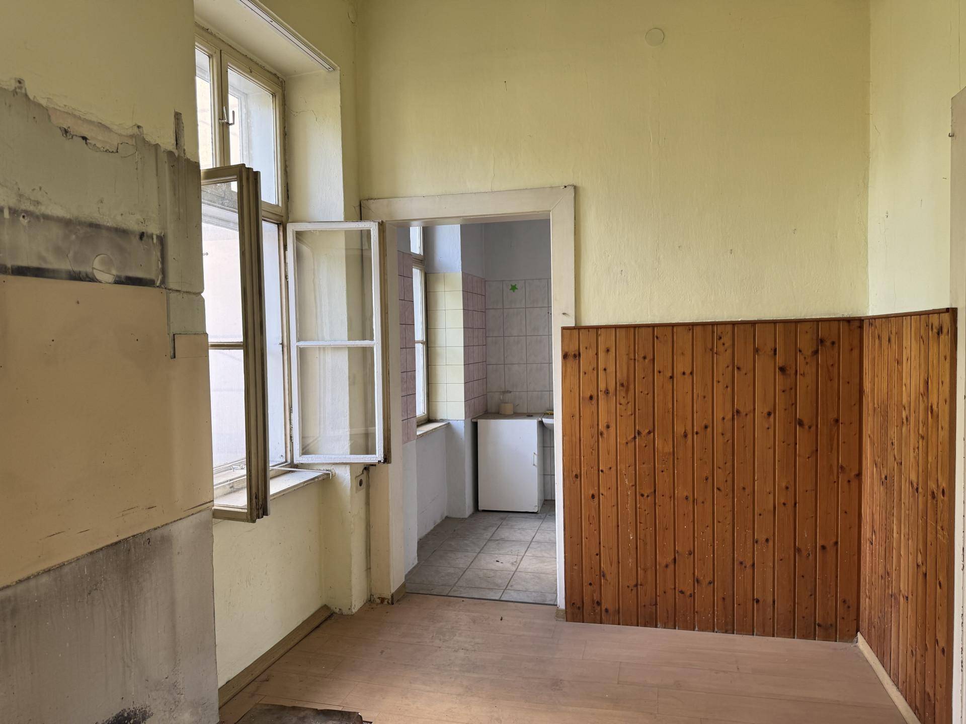 Zimmer mit Holzvertäfelung und Blick in einen gefliesten Nebenraum mit Kühlschrank.
