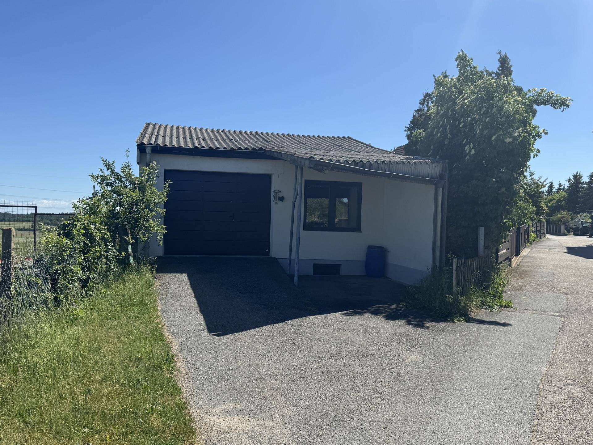 Freistehende Garage mit schwarzem Tor und Zufahrt, umgeben von Grünflächen unter blauem Himmel.