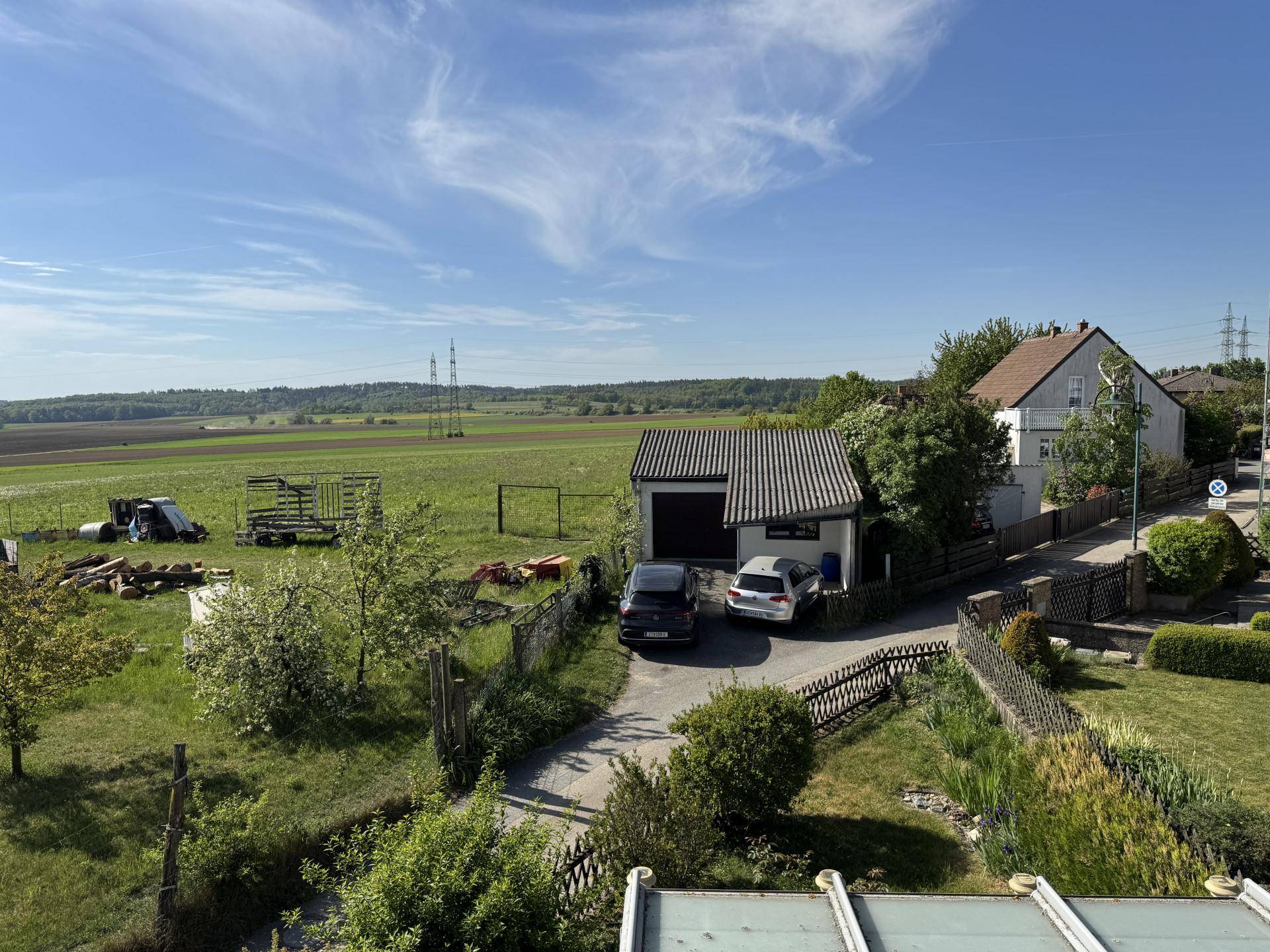 Weitblick über das Anwesen mit Garage, Zufahrt und angrenzenden Feldern unter blauem Himmel.