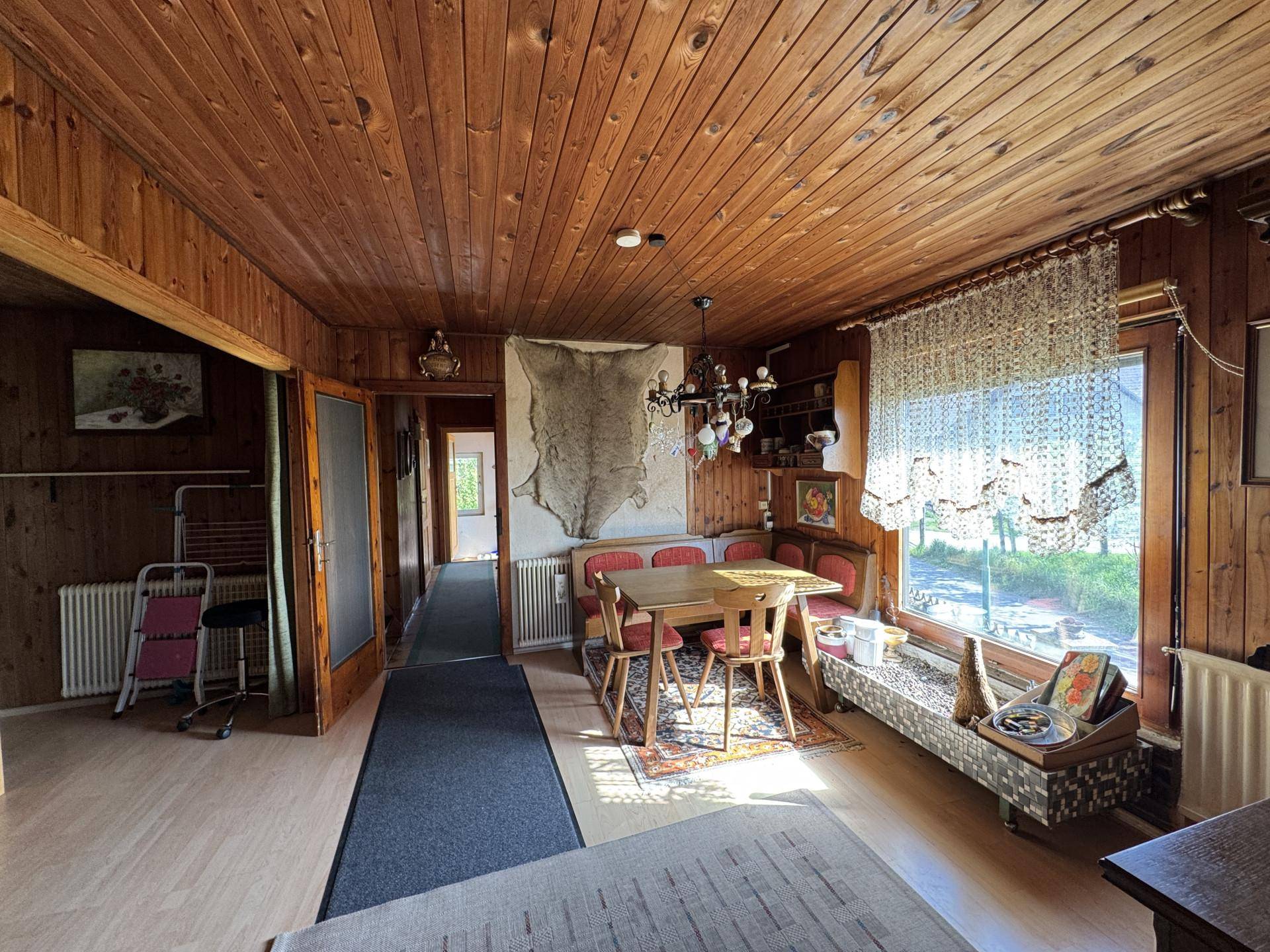 Rustikaler Wohn-Essbereich mit Holzvertäfelung, großem Fenster und traditionellen Möbeln.