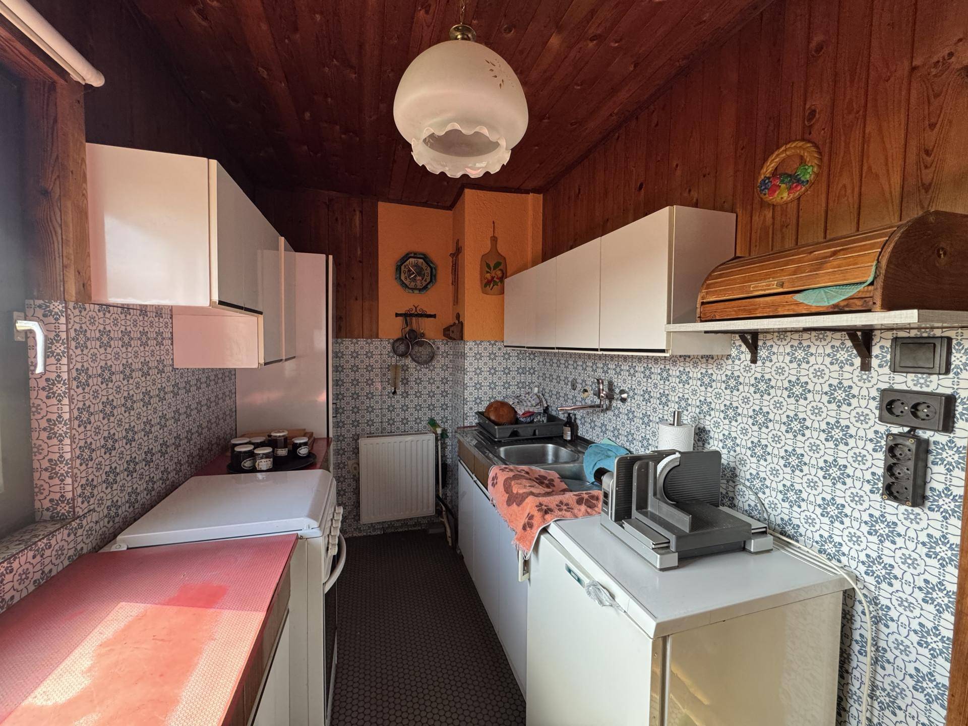 Kleine Küche im Landhausstil mit gemusterten Fliesen, Holzdecke und älteren Geräten.
