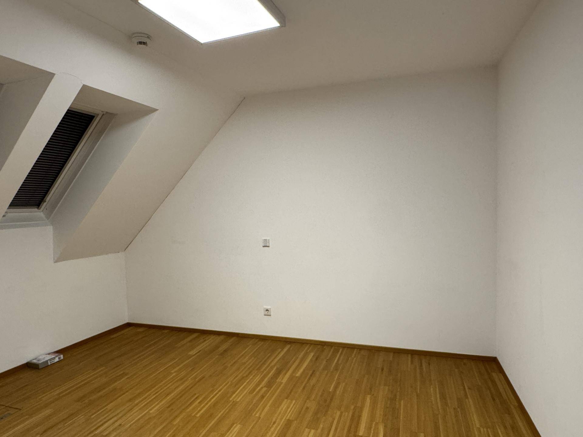 Heller Raum mit Holzboden und einer Dachschräge, ausgestattet mit einem Dachfenster.