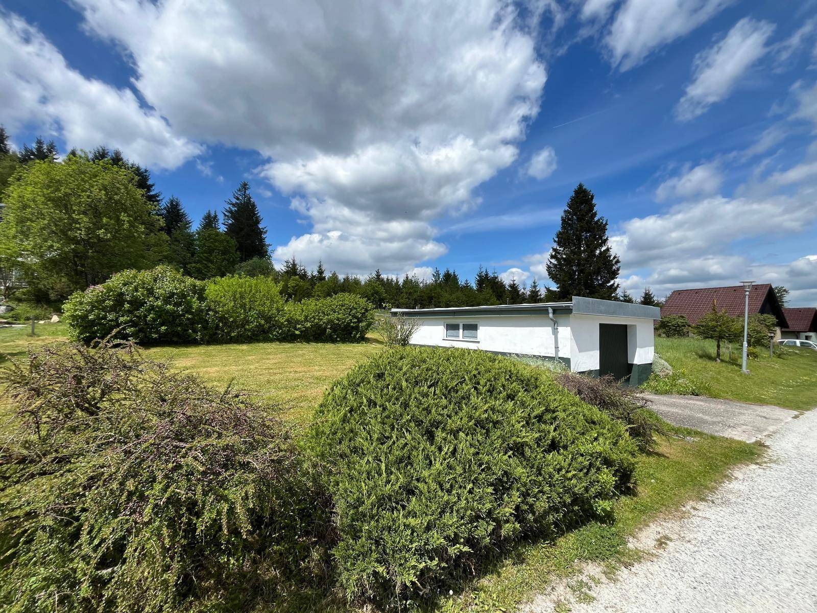 Freistehende Garage in ländlicher Umgebung mit viel Grün und Bäumen unter blauem Himmel.