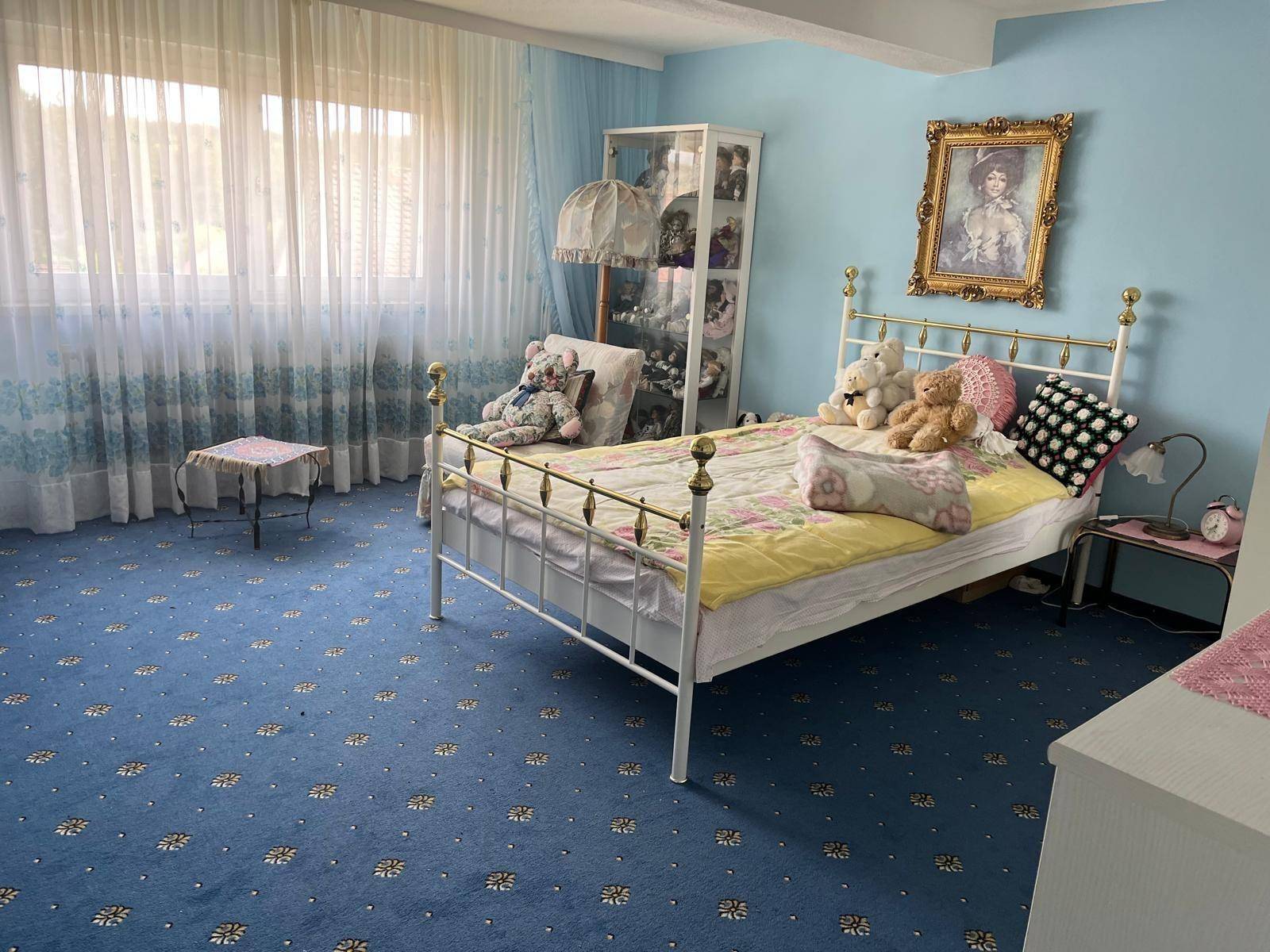 Schlafzimmer mit blauem Teppichboden, Einzelbett und großen Fenstern für viel Licht.