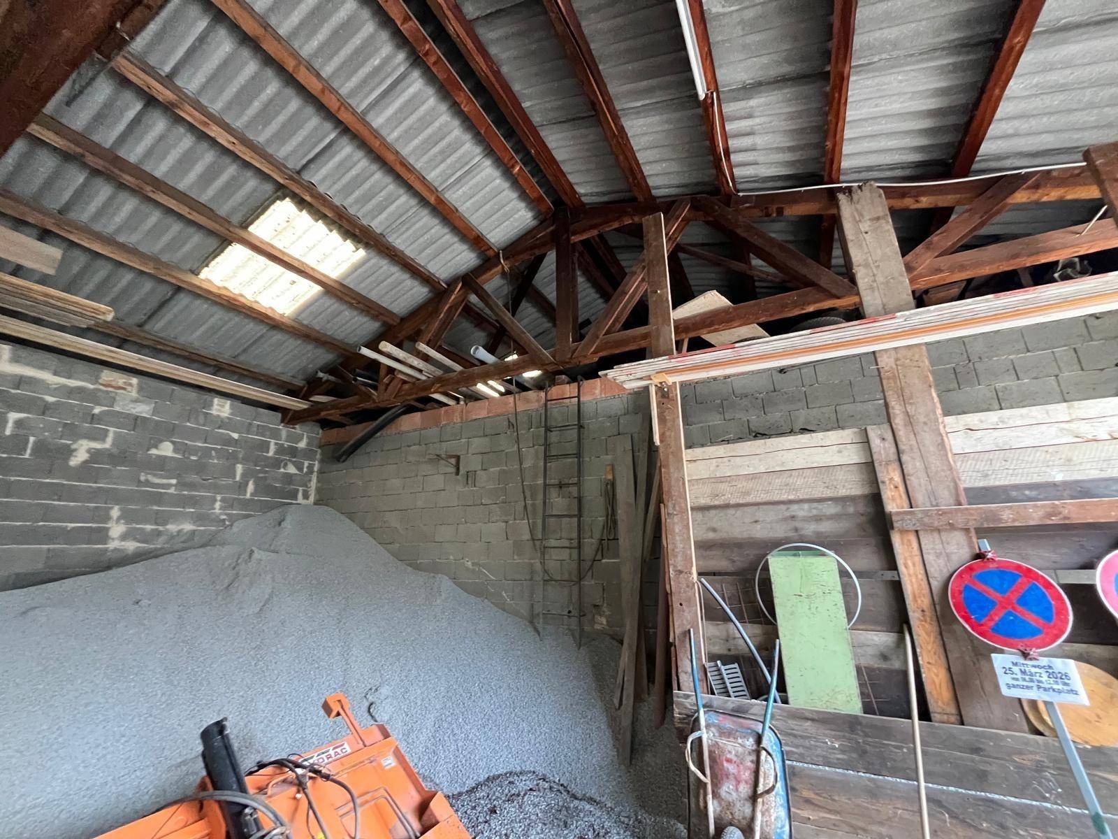 Großer Lagerraum mit sichtbarer Holzkonstruktion des Daches, Wellblechdach und einem großen Haufen Schüttgut.