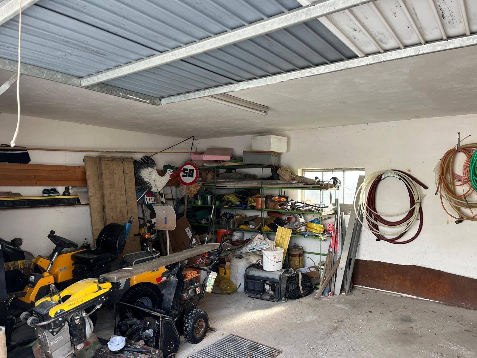 Innenansicht einer Garage oder Werkstatt mit verschiedenen Geräten, Werkzeugen und einer Metallkonstruktion an der Decke.