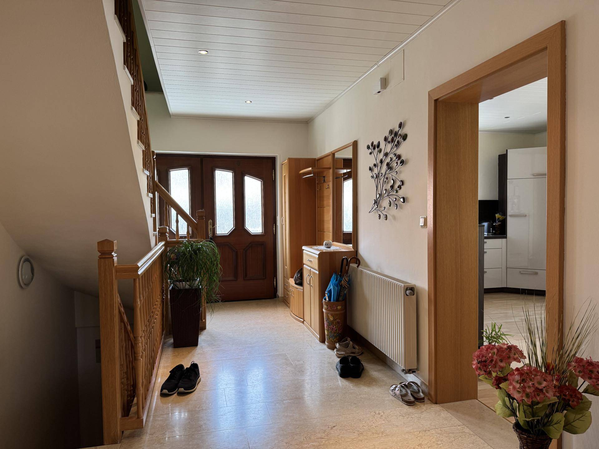 Heller Eingangsbereich mit Fliesenboden, Holztreppe und Garderobe.