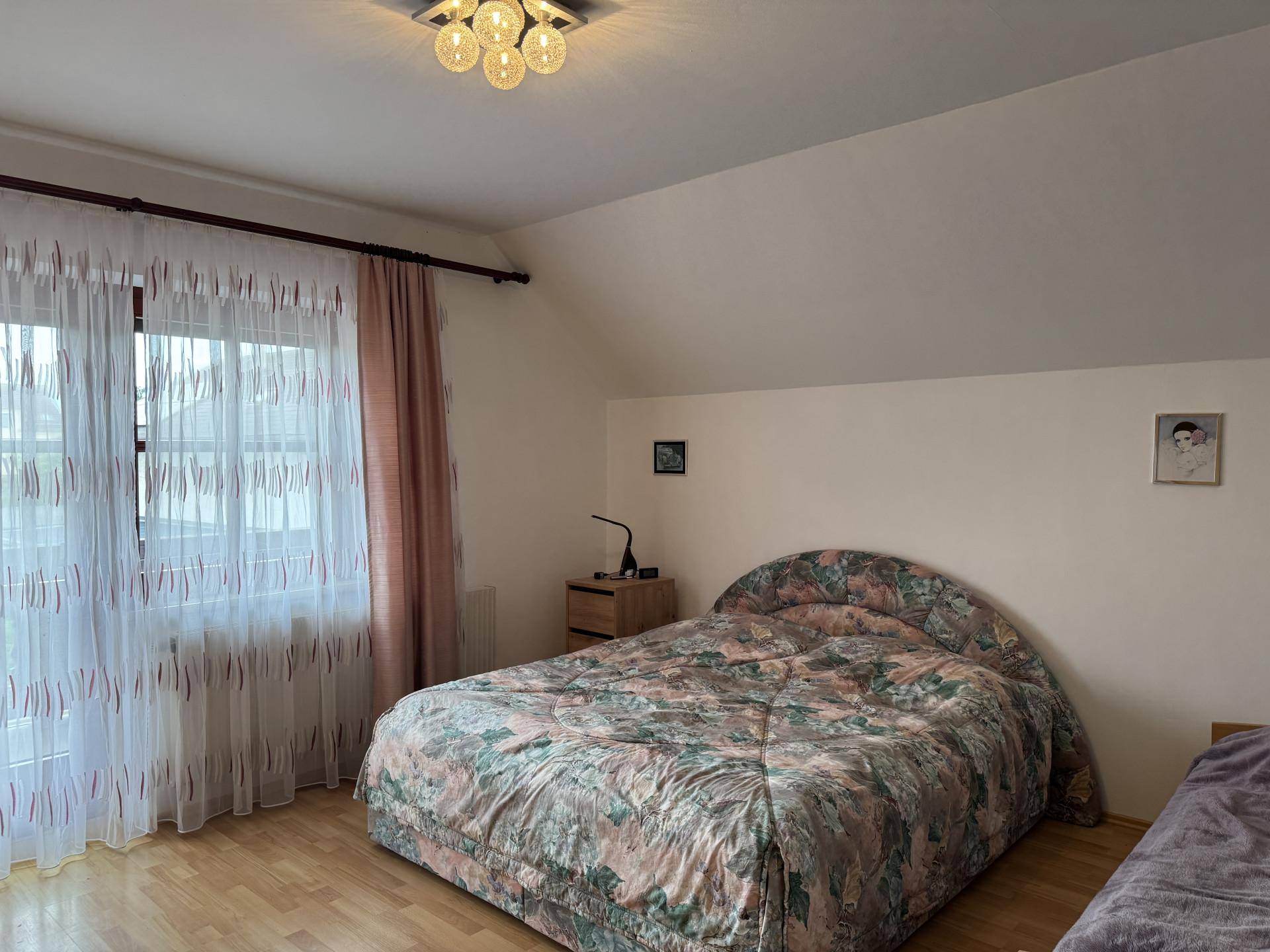 Schlafzimmer mit Doppelbett, Dachschräge und Fenster mit Vorhängen.