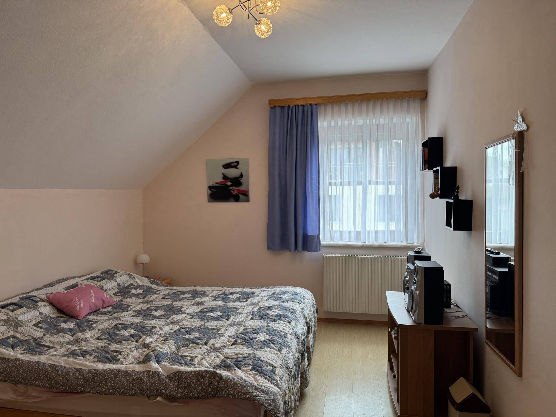 Schlafzimmer mit Dachschräge, Fenster, Heizkörper und einfacher Einrichtung.