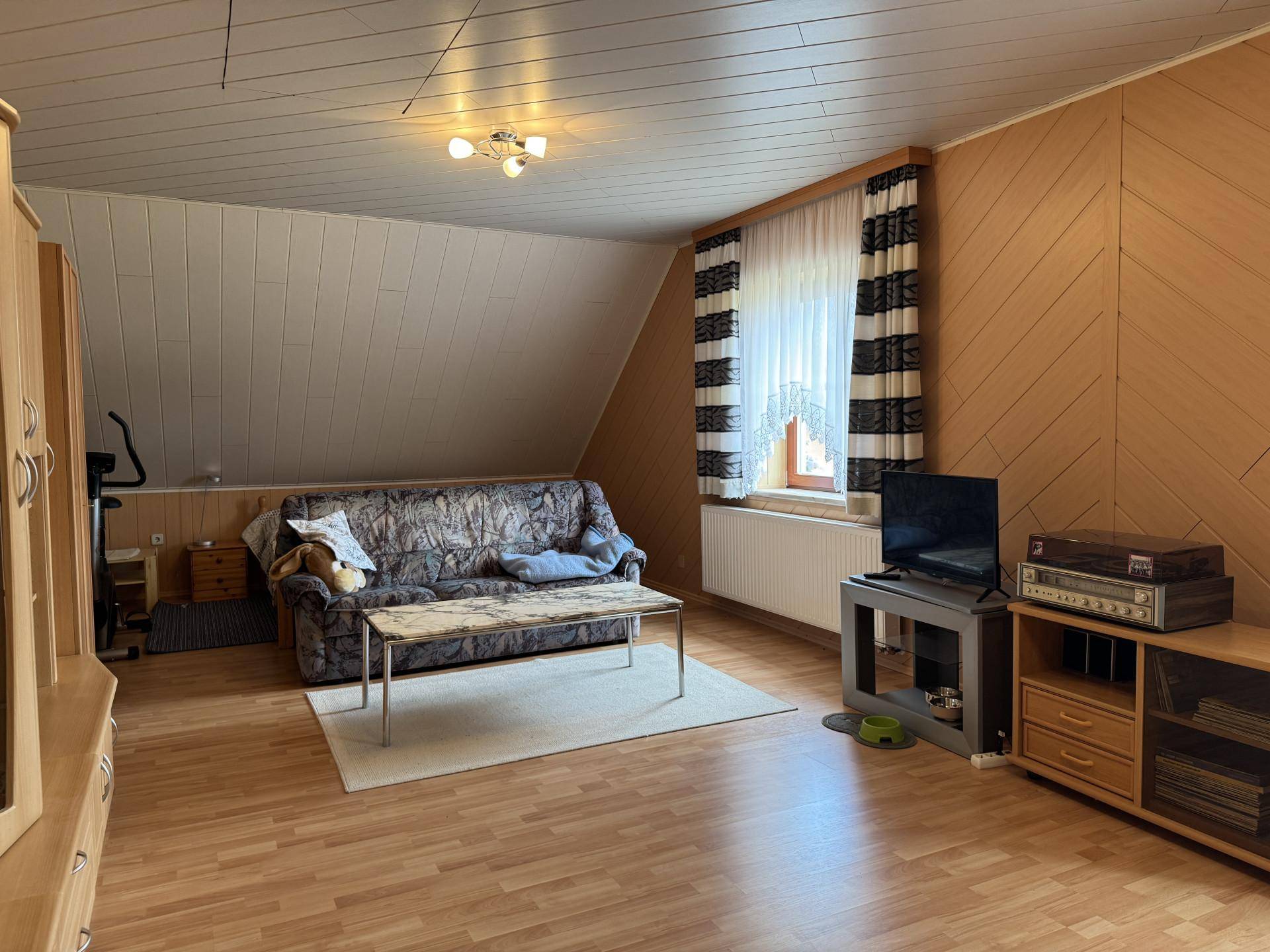 Geräumiger Wohnbereich im Dachgeschoss mit Sofa und Holzverkleidung.