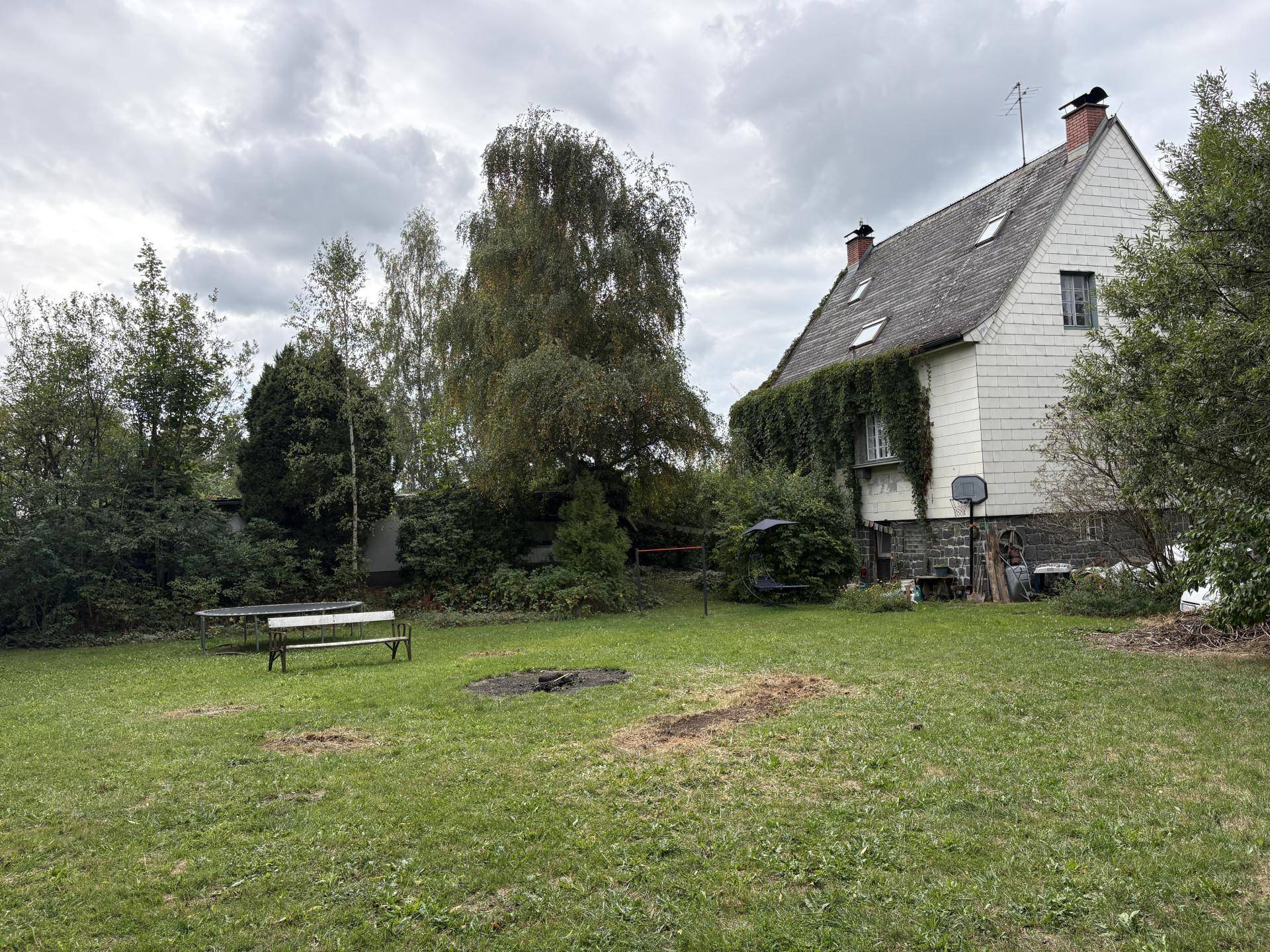 Seitlicher Blick auf das Haus und den weitläufigen Garten mit Rasen und Feuerstelle.