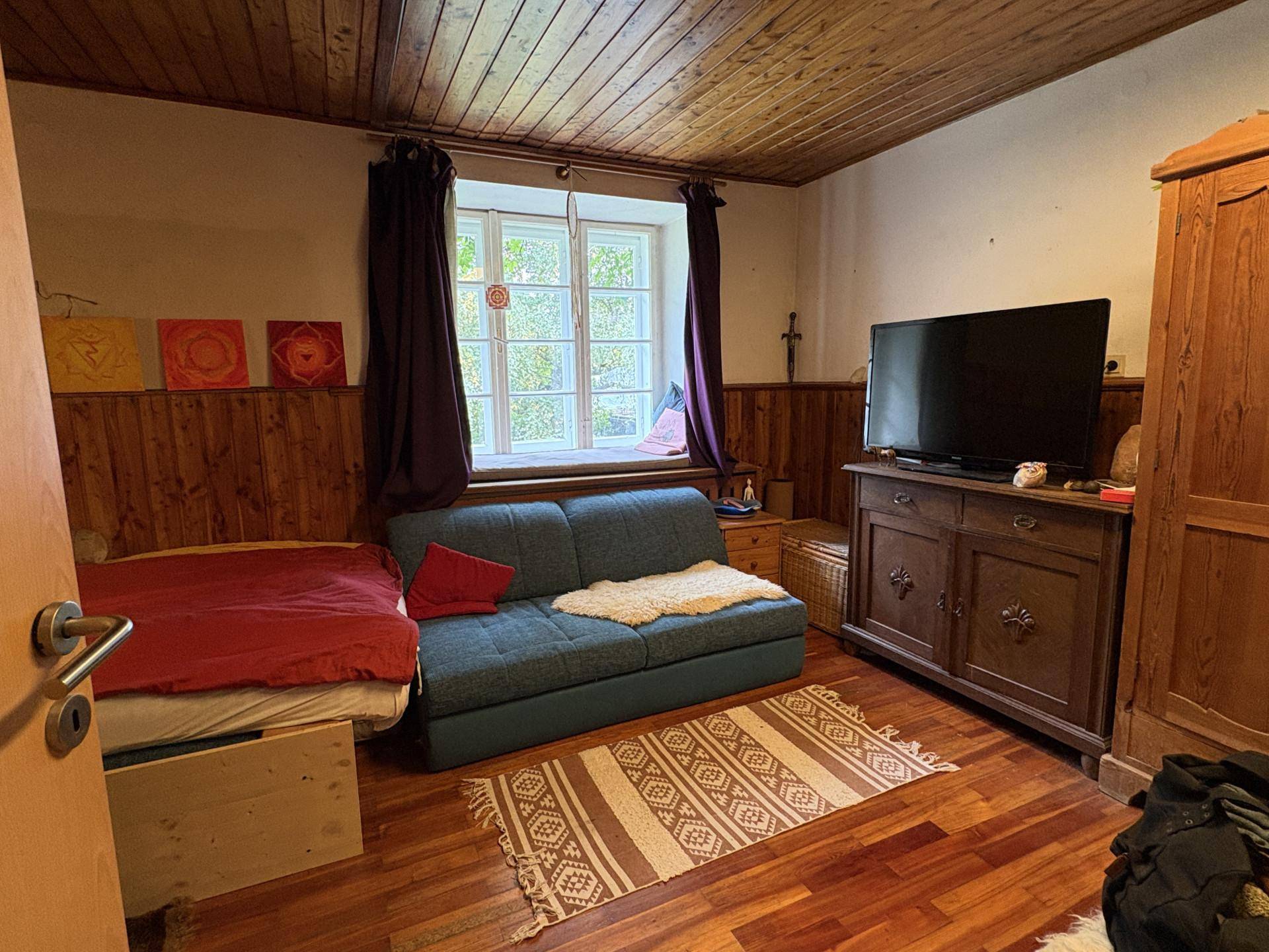Schlafzimmer mit Holzvertäfelung, einem Bett, Schlafsofa und Fernseher auf einem Holzschrank.