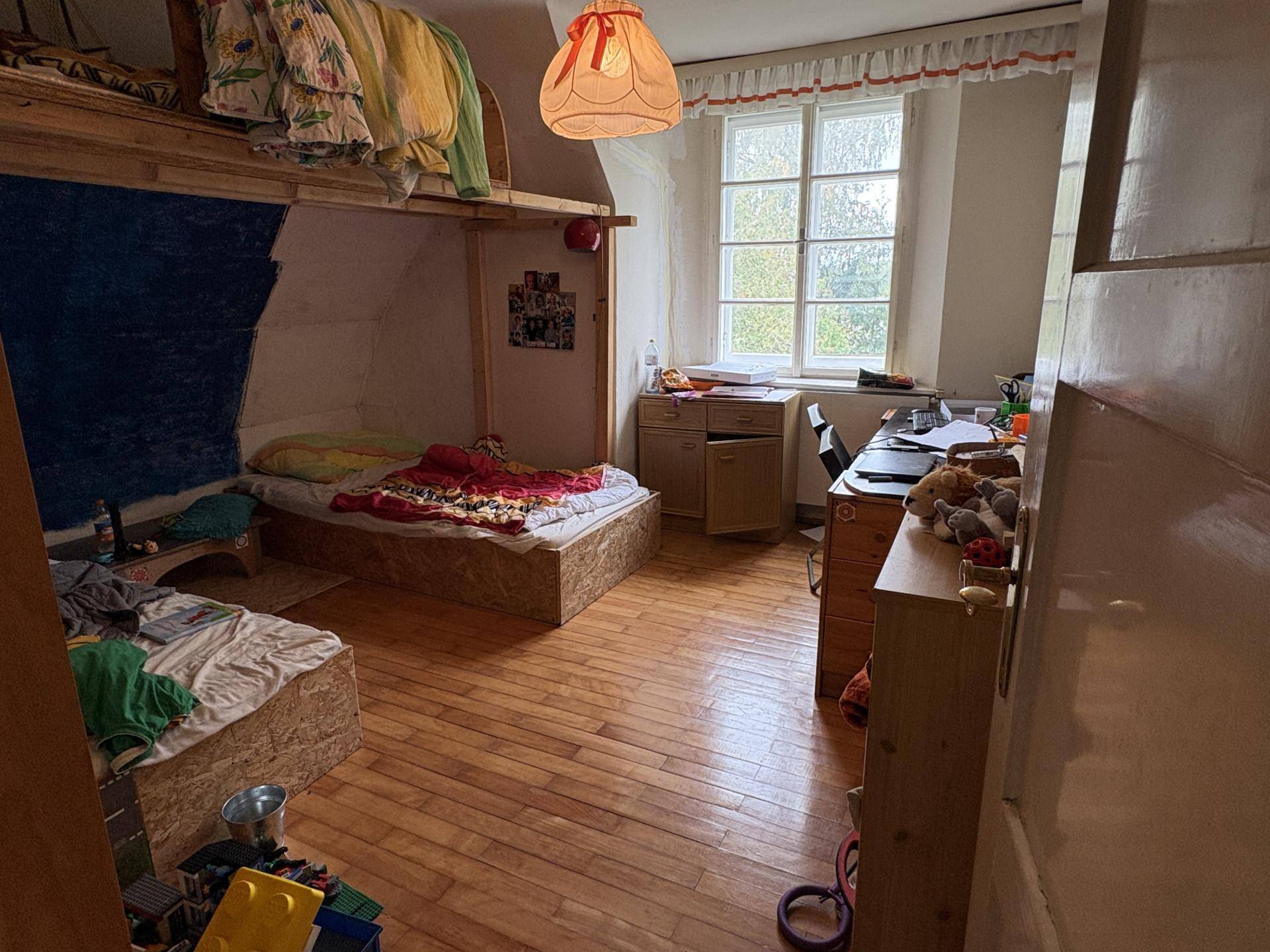 Kinderzimmer mit Holzboden, Etagenbetten und einem Schreibtisch am Fenster.