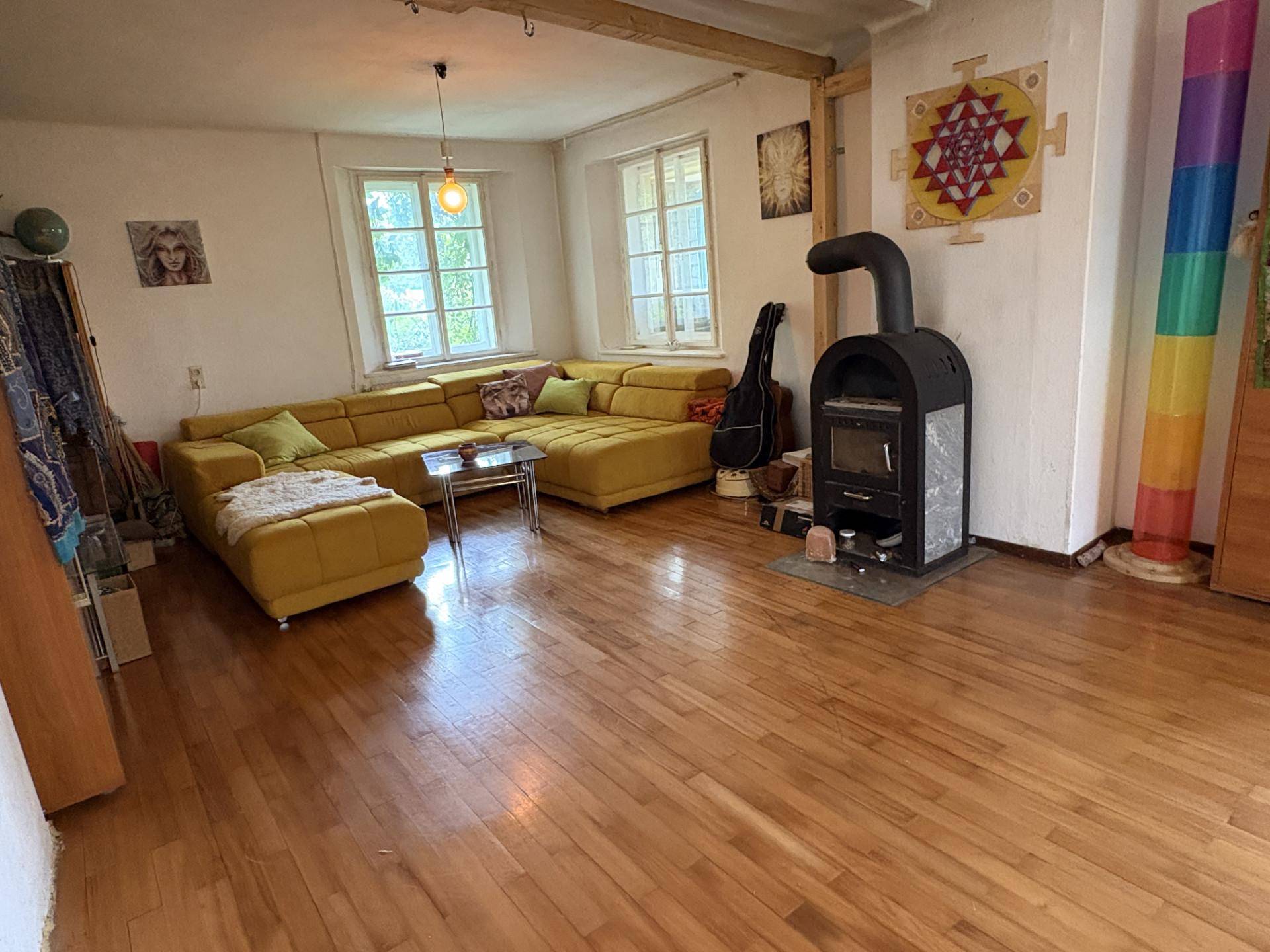 Geräumiges Wohnzimmer mit Holzboden, großer gelber Couch und einem gemütlichen Holzofen.