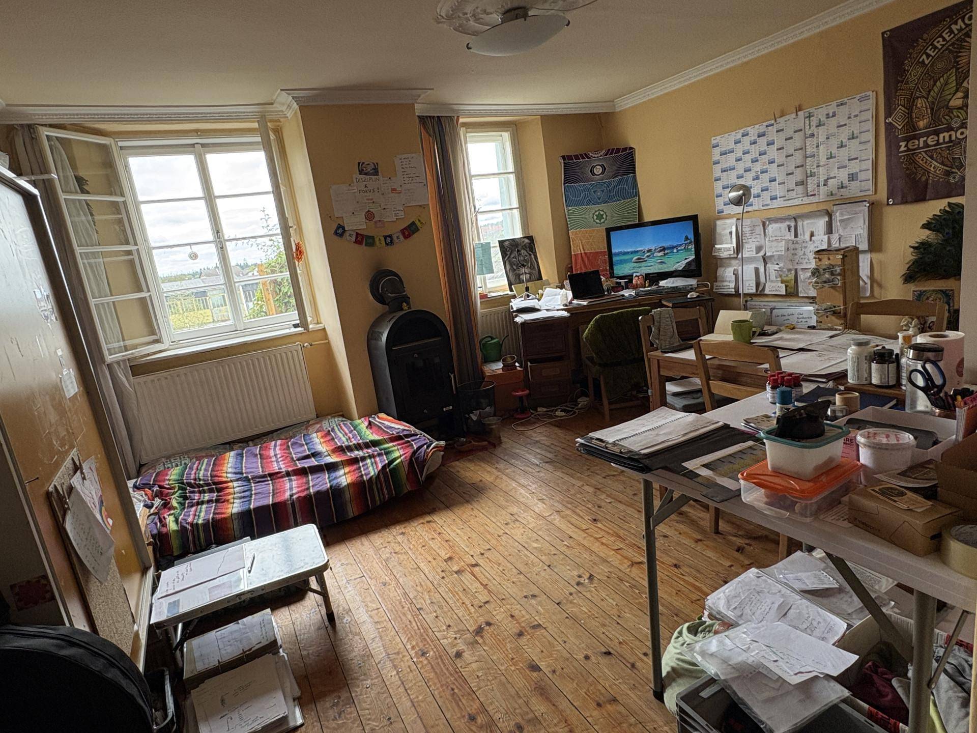 Helles Arbeitszimmer mit Holzboden, einem Bett und einem weiteren Holzofen.