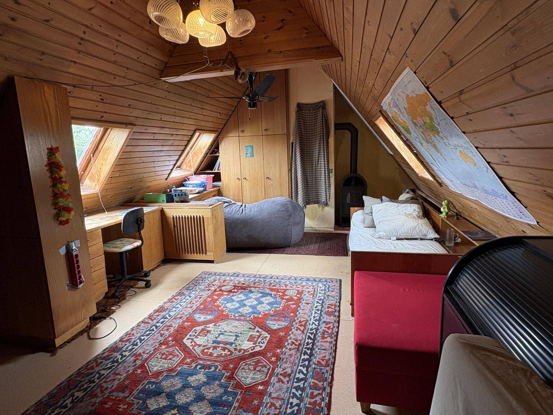 Gemütliches Dachzimmer mit Holzverkleidung, Schrägen, Bett und Arbeitsbereich.