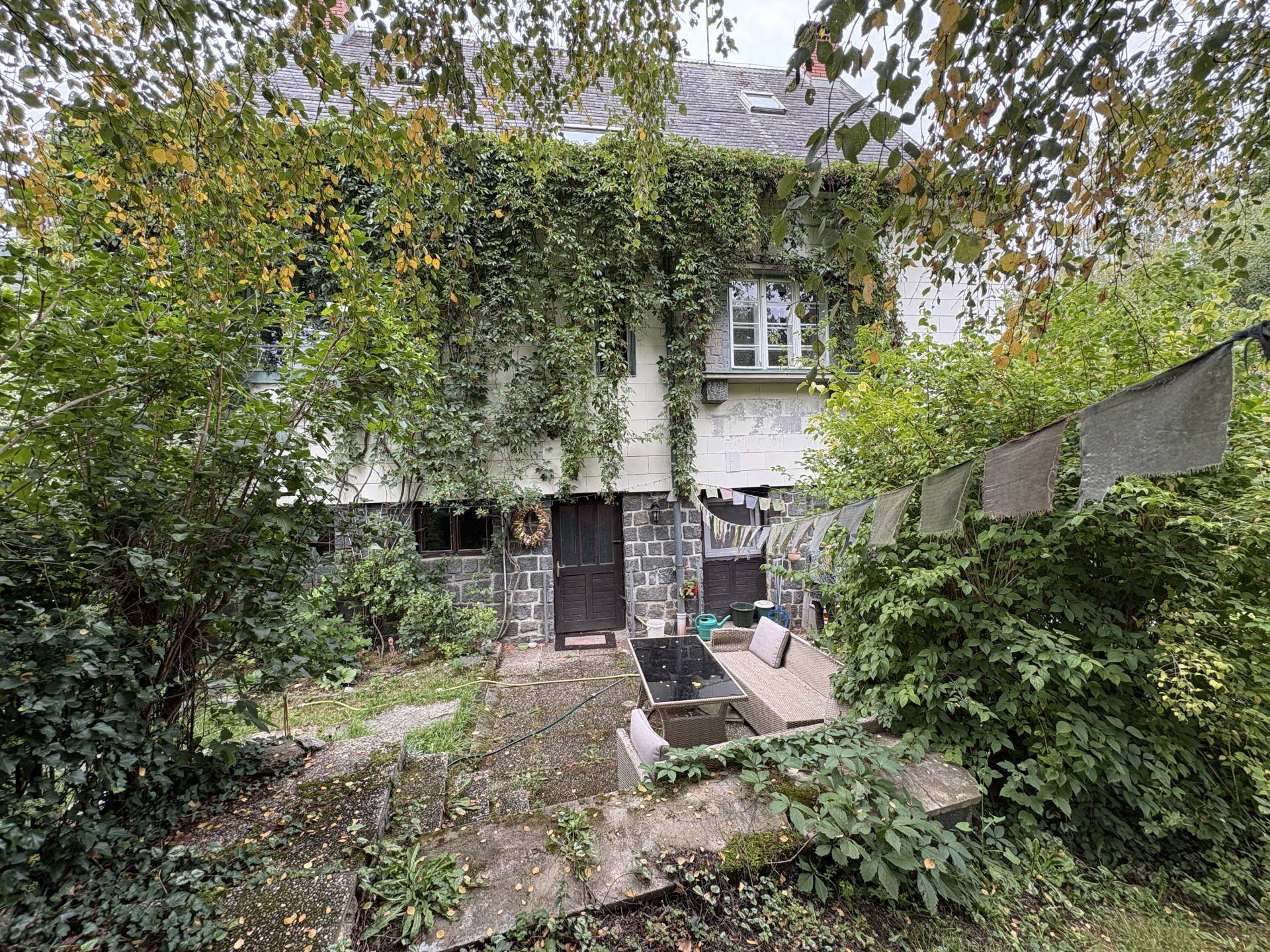 Rückseite des Hauses mit Efeu, einer kleinen Terrasse und gemütlicher Sitzgelegenheit im Freien.
