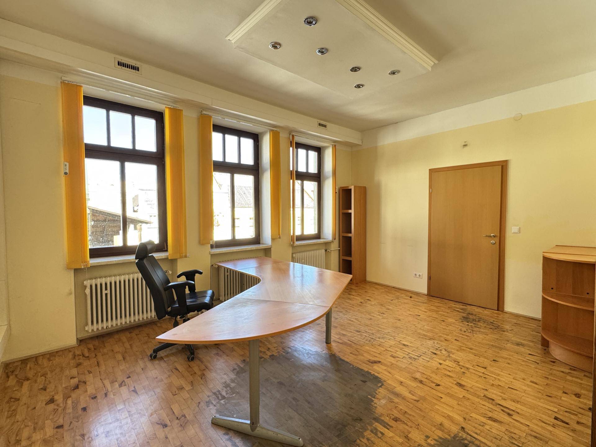 Großes Büro mit Parkettboden, einem geschwungenen Schreibtisch und mehreren Fenstern für Tageslicht.