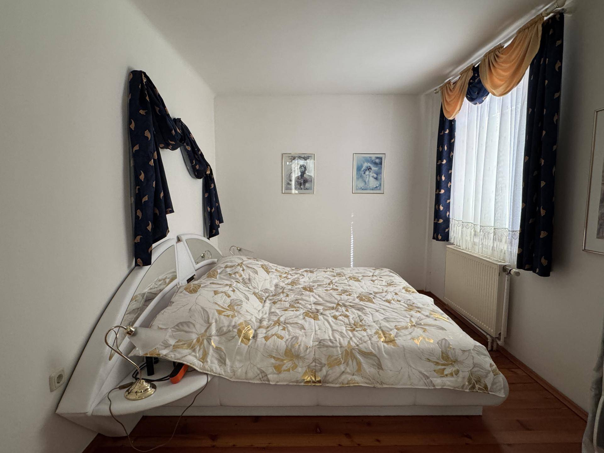 Schlafzimmer mit Doppelbett, Holzboden und Vorhängen am Fenster für Privatsphäre.
