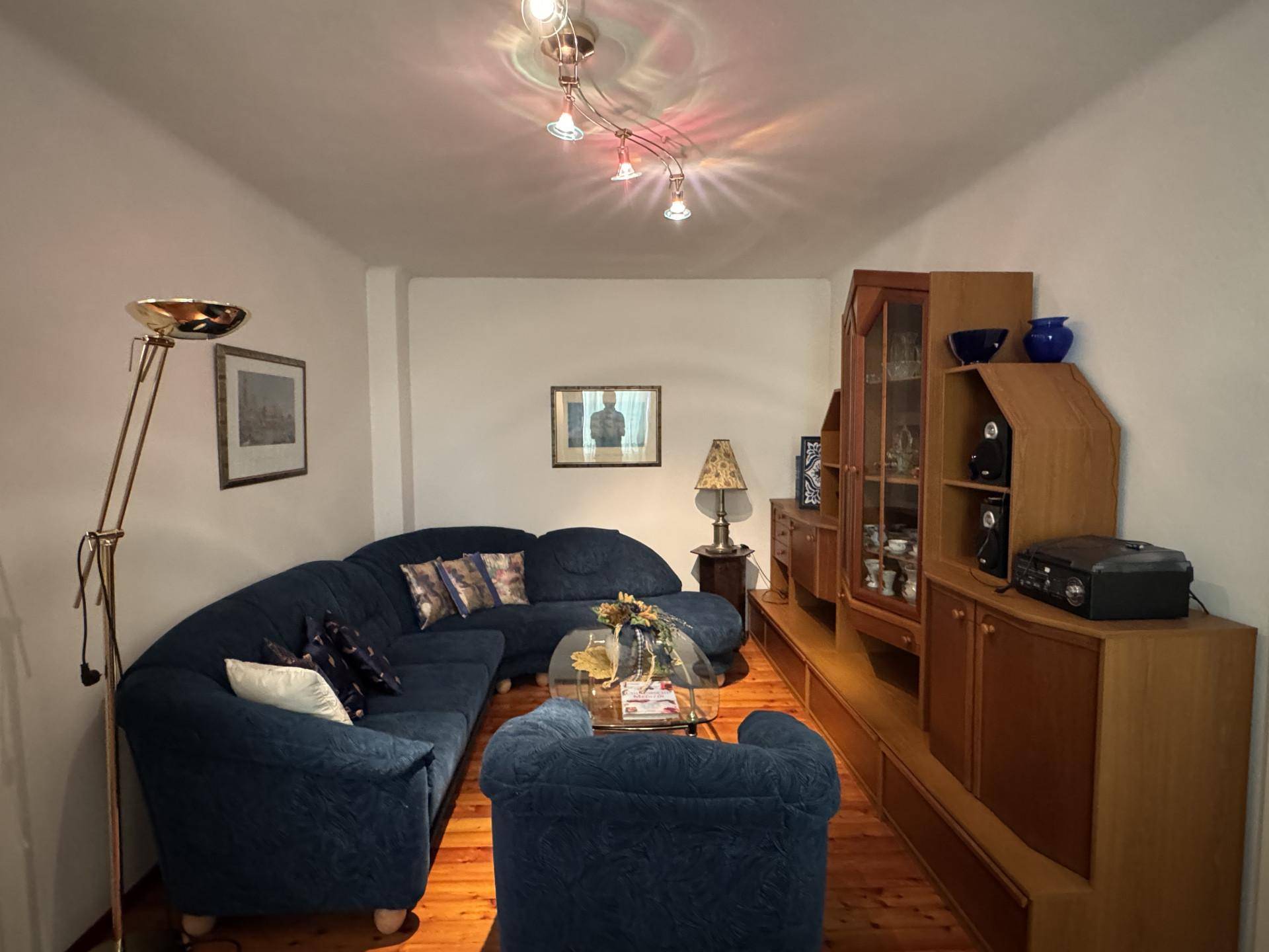Gemütliches Wohnzimmer mit blauer Eckcouch, Holzmöbeln und Deckenleuchten.