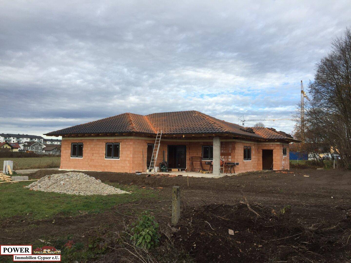 Einfamilienhaus im Rohbau mit Ziegeldach und Baustelle im Vordergrund.