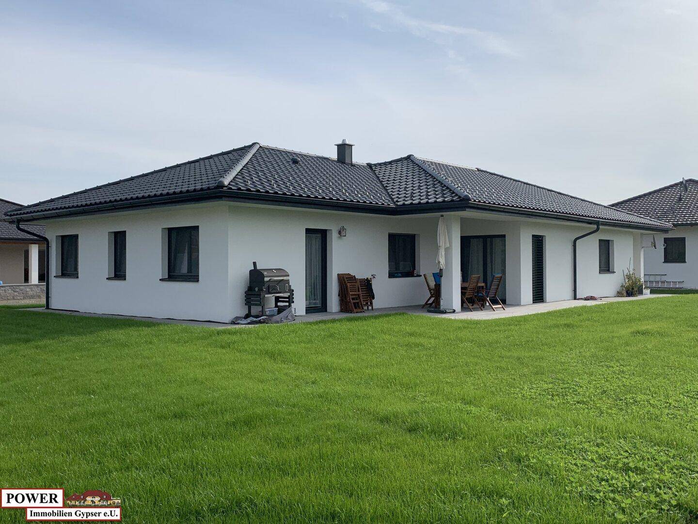 Rückseite eines modernen Einfamilienhauses mit großer Rasenfläche und kleiner Terrasse.