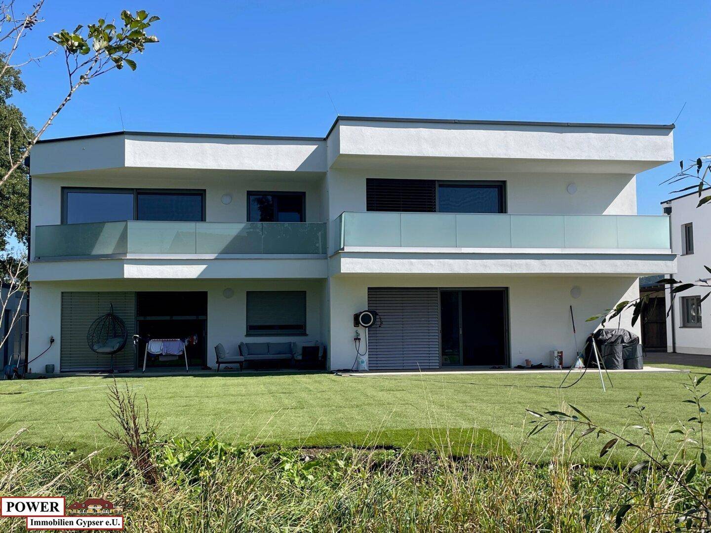 Modernes Mehrfamilienhaus mit großen Balkonen, Glasbrüstungen und gepflegtem Rasen.