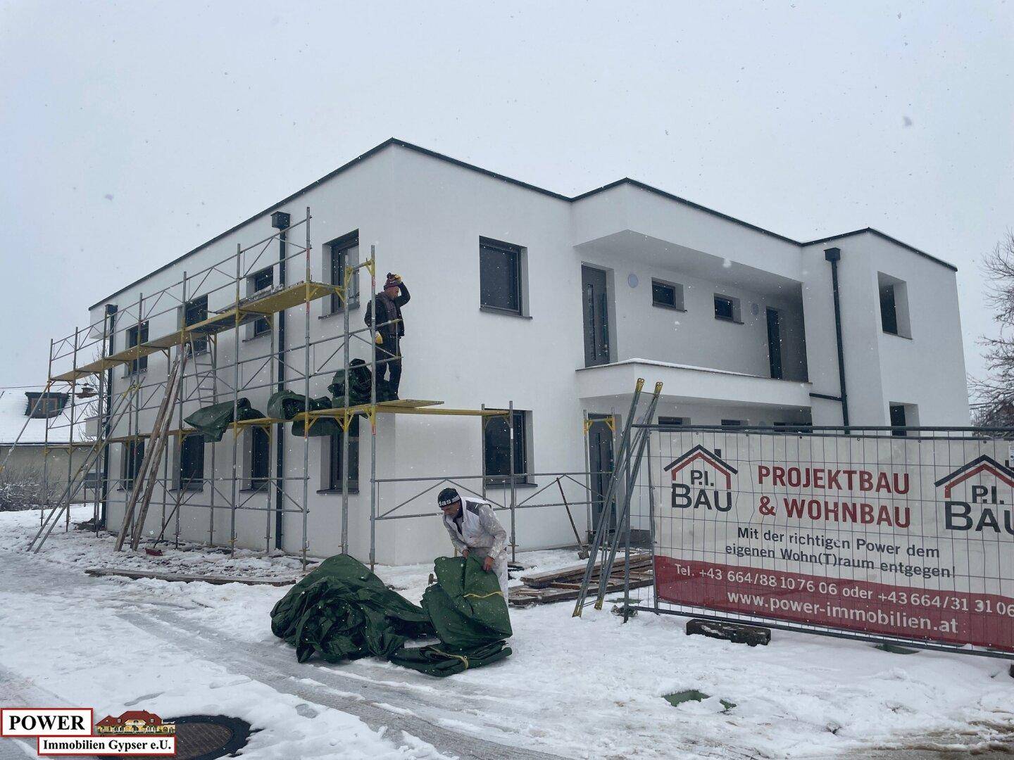 Neubau mit weißer Fassade und Gerüst, umgeben von Schnee, kurz vor der Fertigstellung.