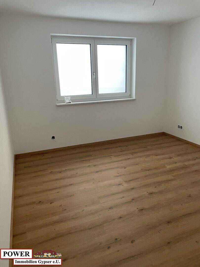 Leeres Schlafzimmer mit Laminatboden und einem großen Fenster für viel Tageslicht.