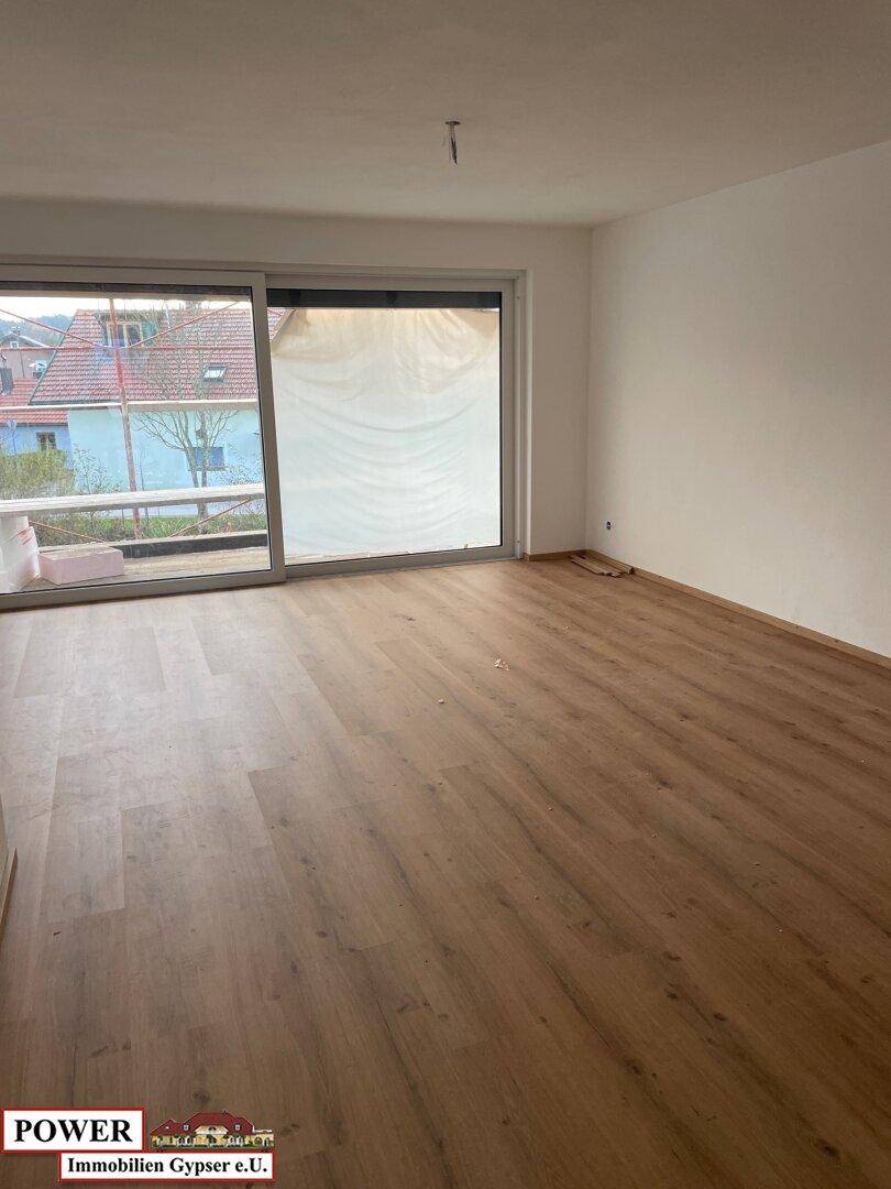 Geräumiges Wohnzimmer mit Laminatboden und Zugang zu einem Balkon oder einer Terrasse.