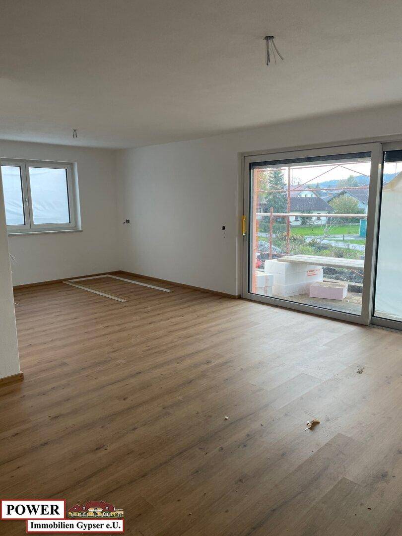 Helles Wohnzimmer mit Laminatboden, großen Fenstern und Schiebetür zum Außenbereich.